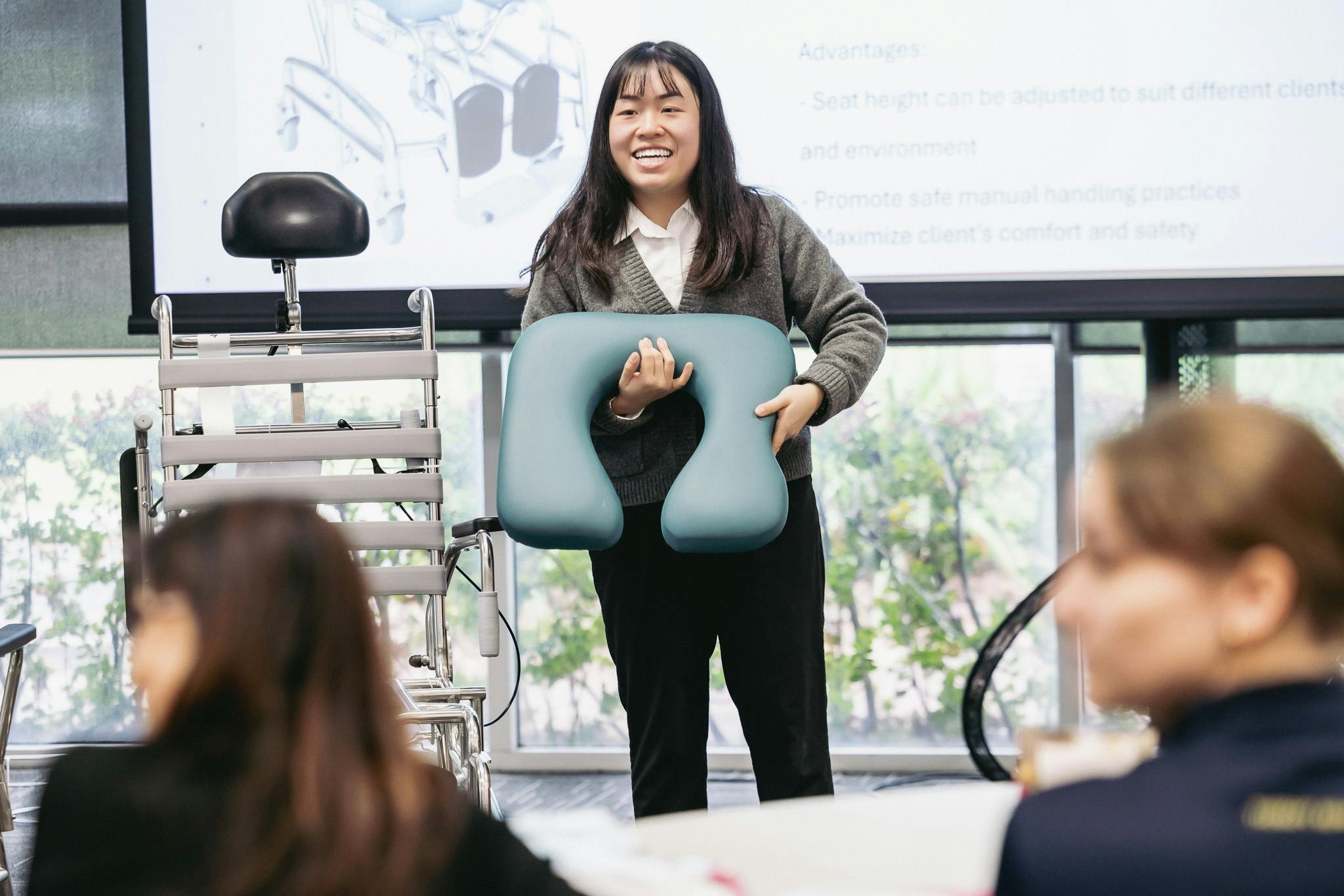clinical educator holds a removable shower commode seat while teaching occupational therapists