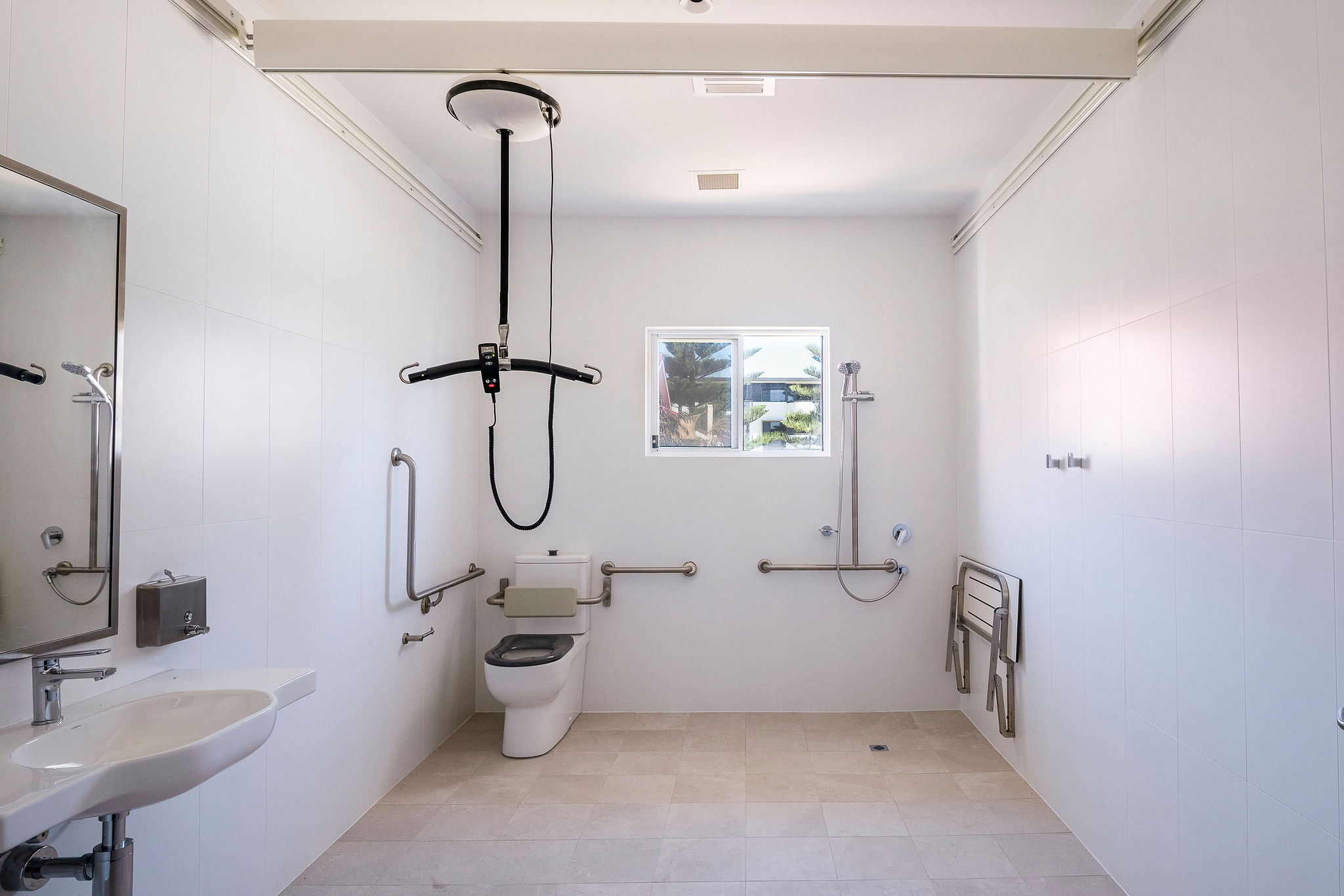 Large accessible bathroom with ceiling hoist, grab rails and roll-in shower at Lady Lawley Cottage Cottesloe, Perth disability accommodation