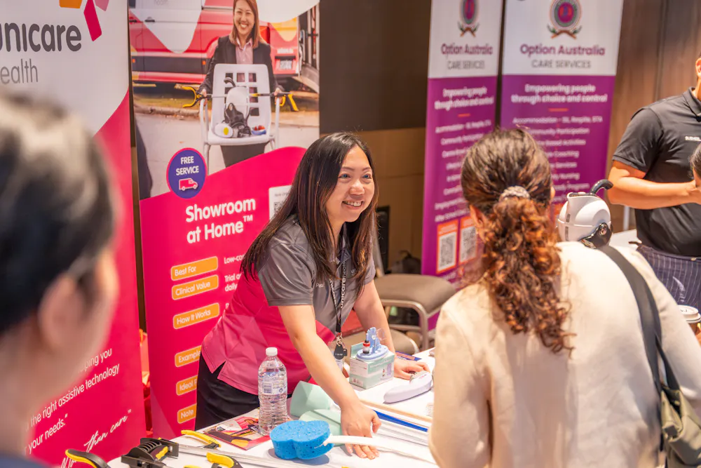 Unicare staff member speaking with attendee at Bankstown Disability Expo NSW, showcasing Showroom at Home service and assistive equipment at Canterbury League Club Belmore