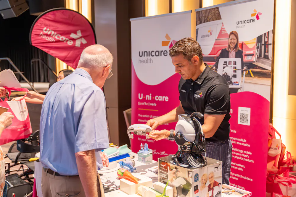 Unicare staff demonstrating assistive equipment to attendee at Bankstown Disability Expo NSW, showcasing Showroom at Home service at Canterbury League Club Belmore