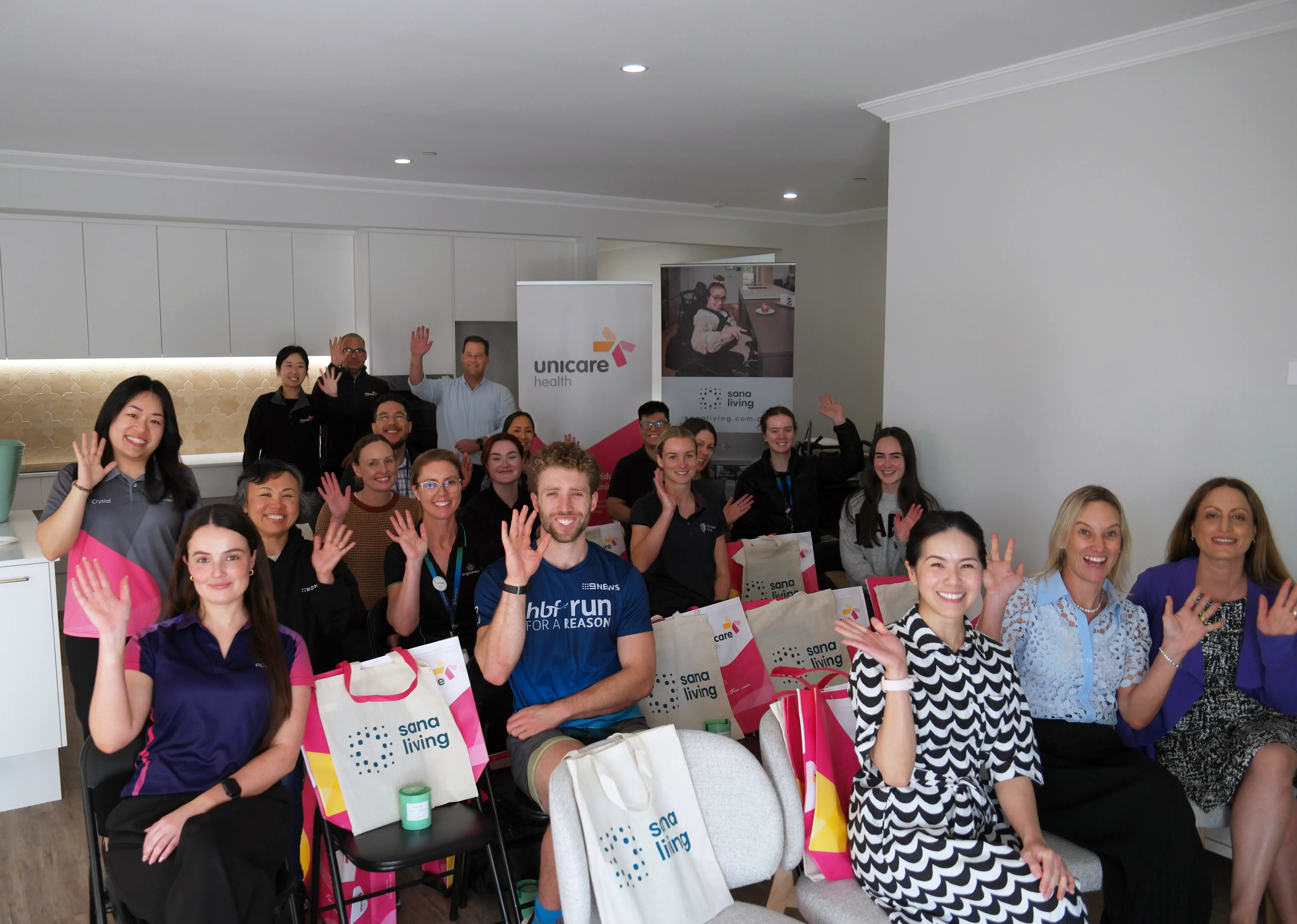 Large group of education event participants smiling and posing together, with Unicare Health promotional bags, at Sana Living in Perth.