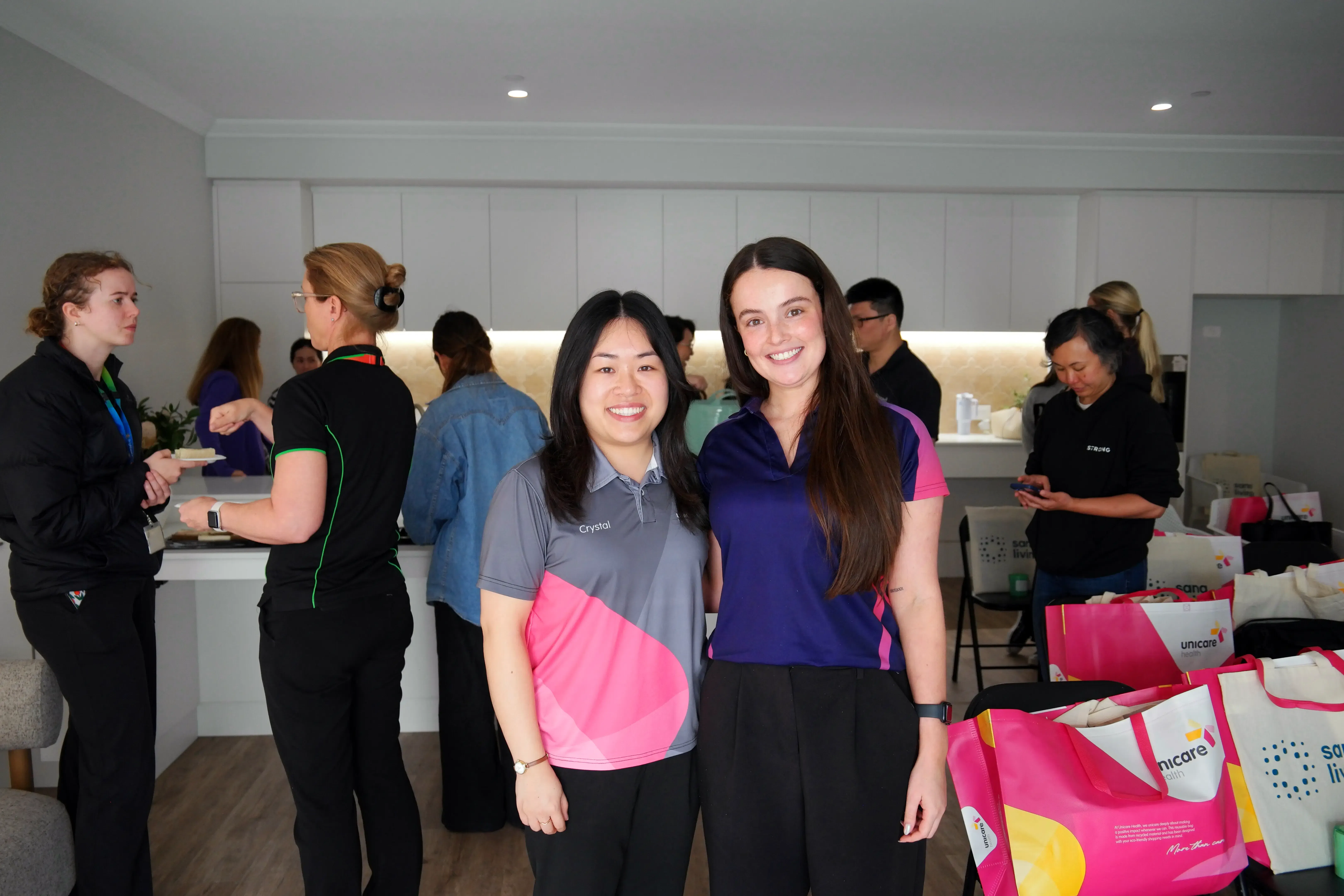 Crystal and an OT from Rocky Bay posing together inside the Sana Living demonstration home, with other event participants in the background.