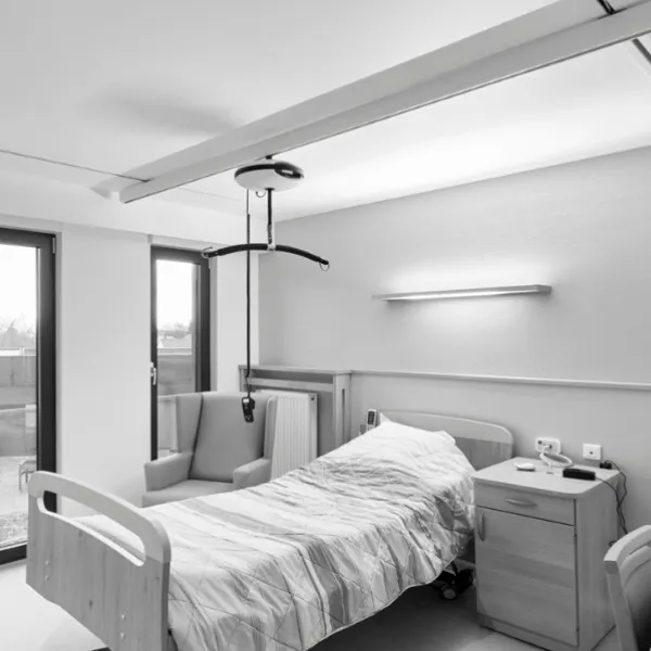 Ceiling hoist suspended from an embedded track above a bedroom care bed.