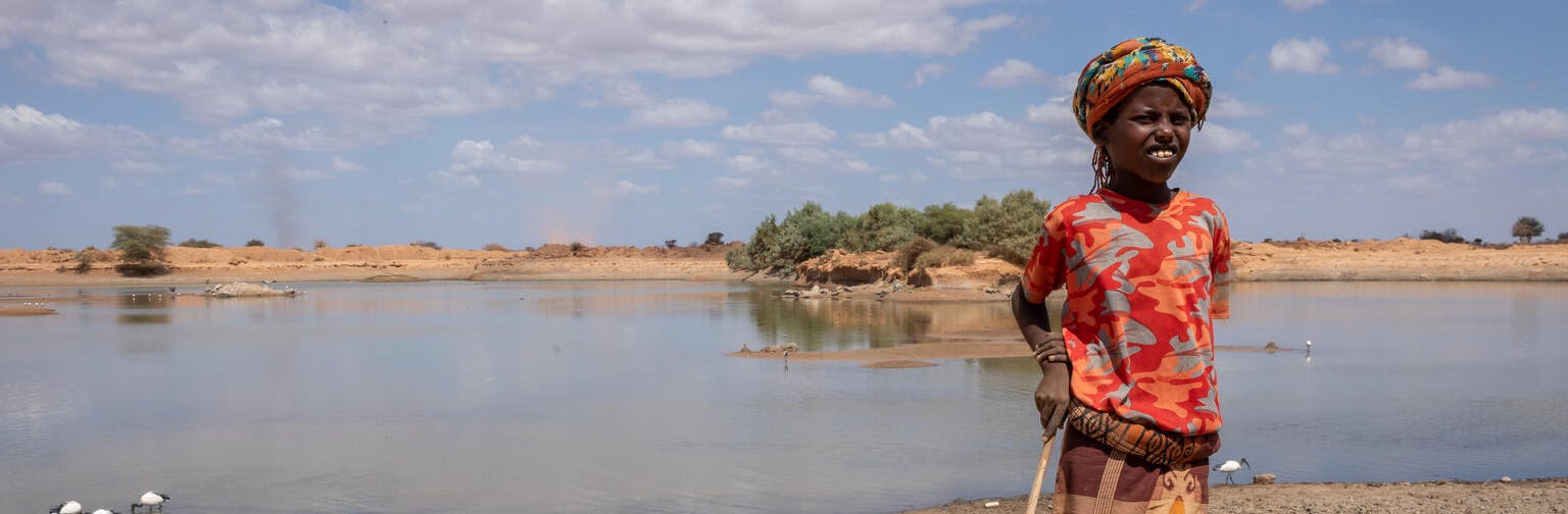 child stands in front of dirty and receding water source
