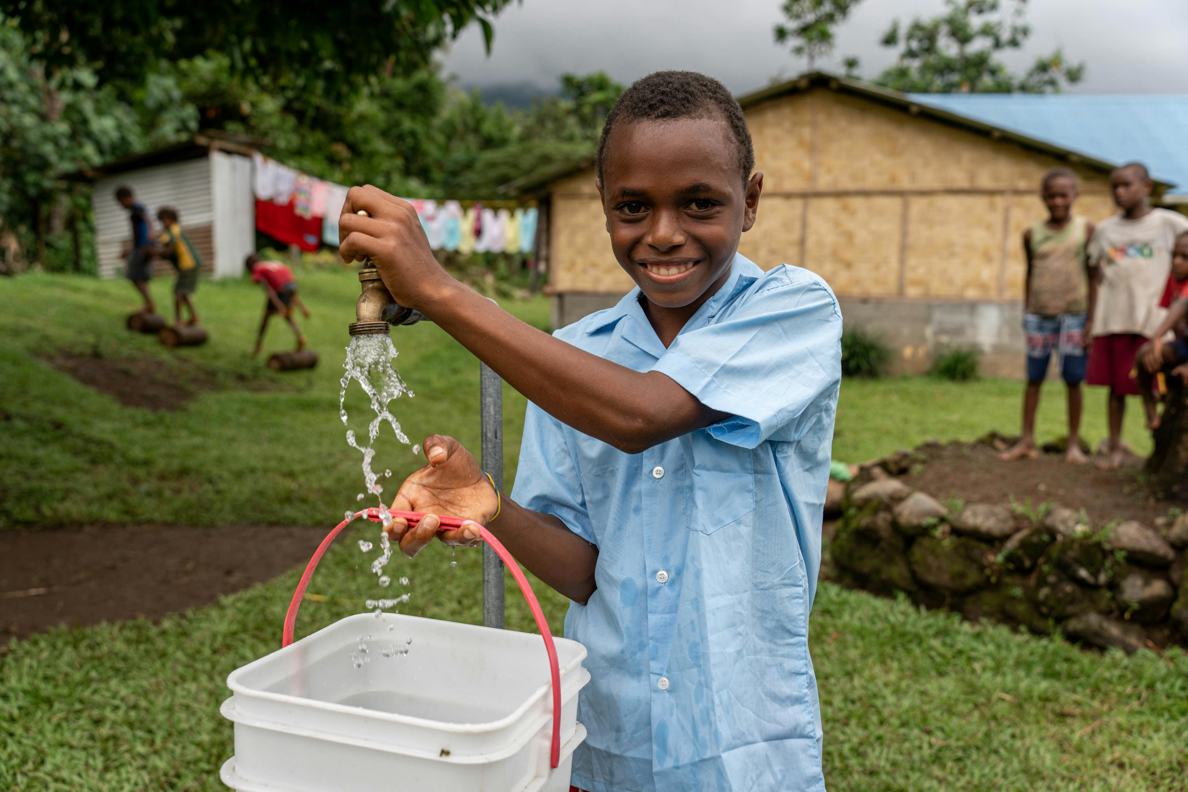 A young boy smiles while collecting clean water from a tap in the Pacific