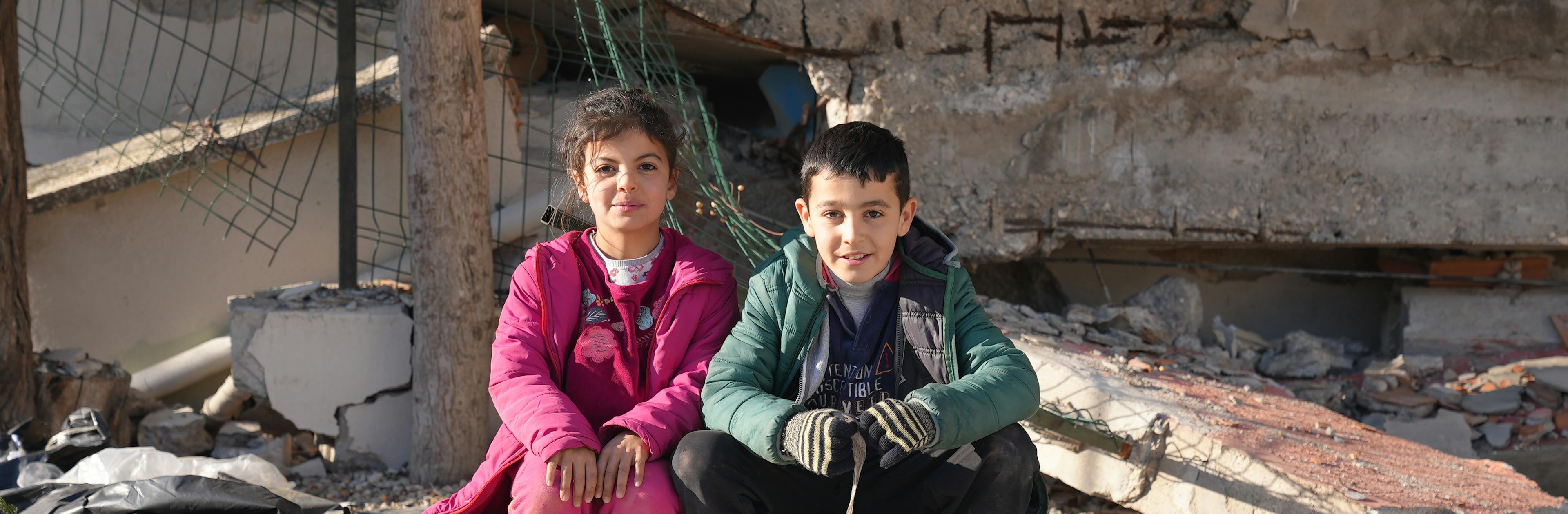Two children sit on the ground outside a destroyed building from the Türkiye and Syria earthquakes