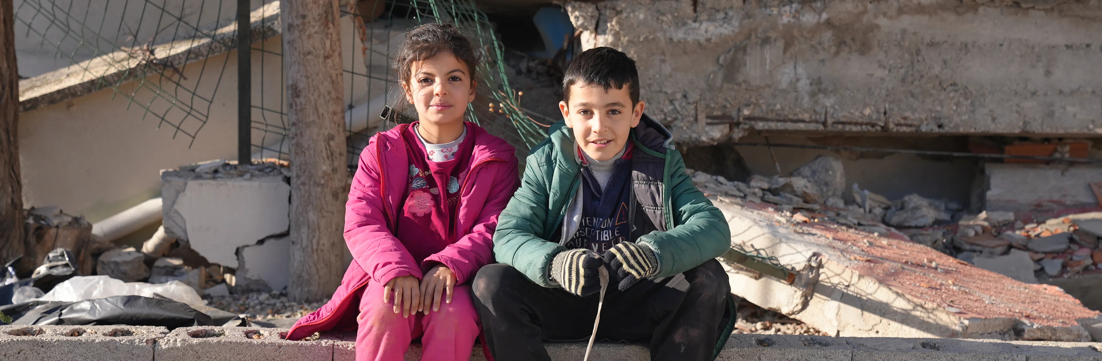 Two children sit on the ground outside a destroyed building from the Türkiye and Syria earthquakes