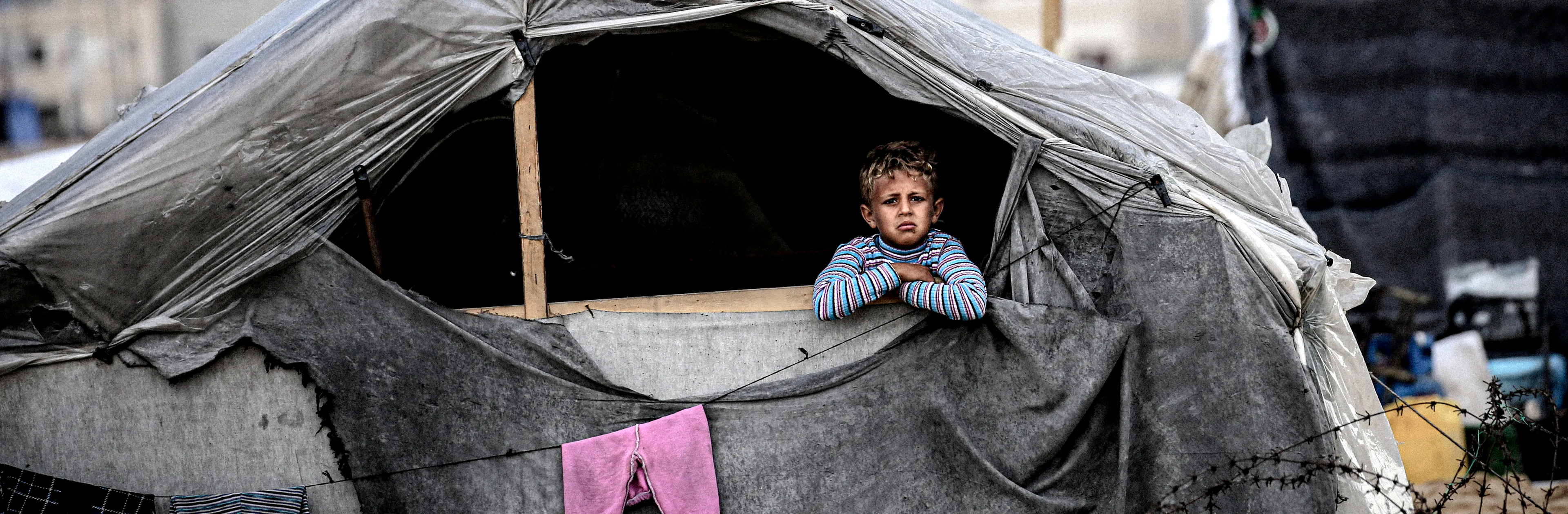 A child peers out from a makeshift shelter built from wood and plastic, where displaced families have sought safety in Rafah, south of the Gaza Strip. 