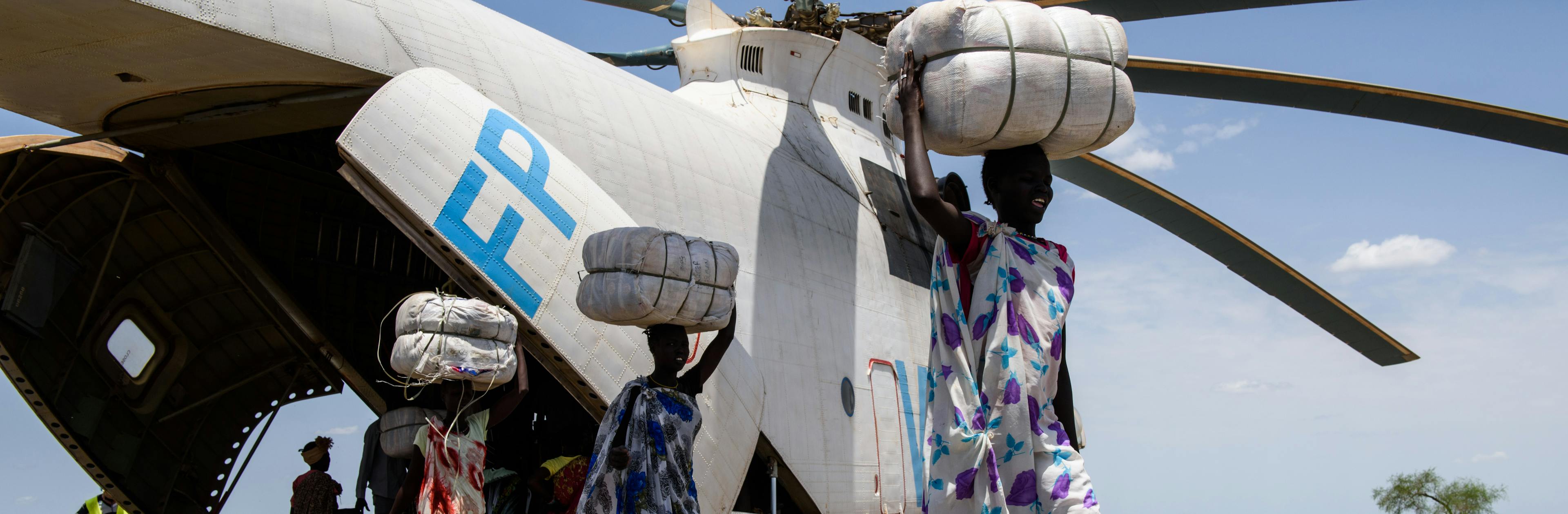 Smiling women carrying UNICEF supplies from a delivery helicopter 