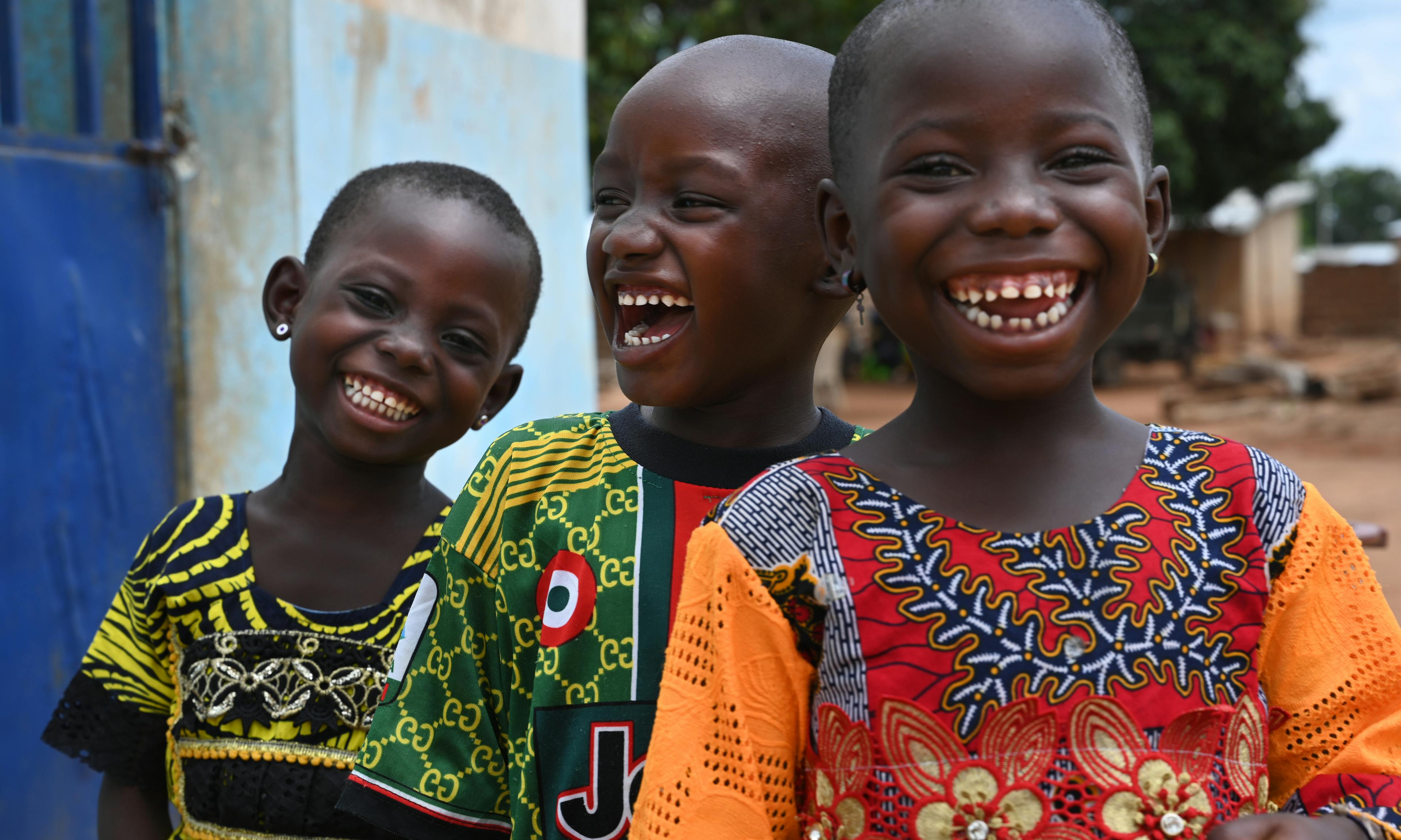 Three young children in colourful dresses are laughing and smiling at the camera