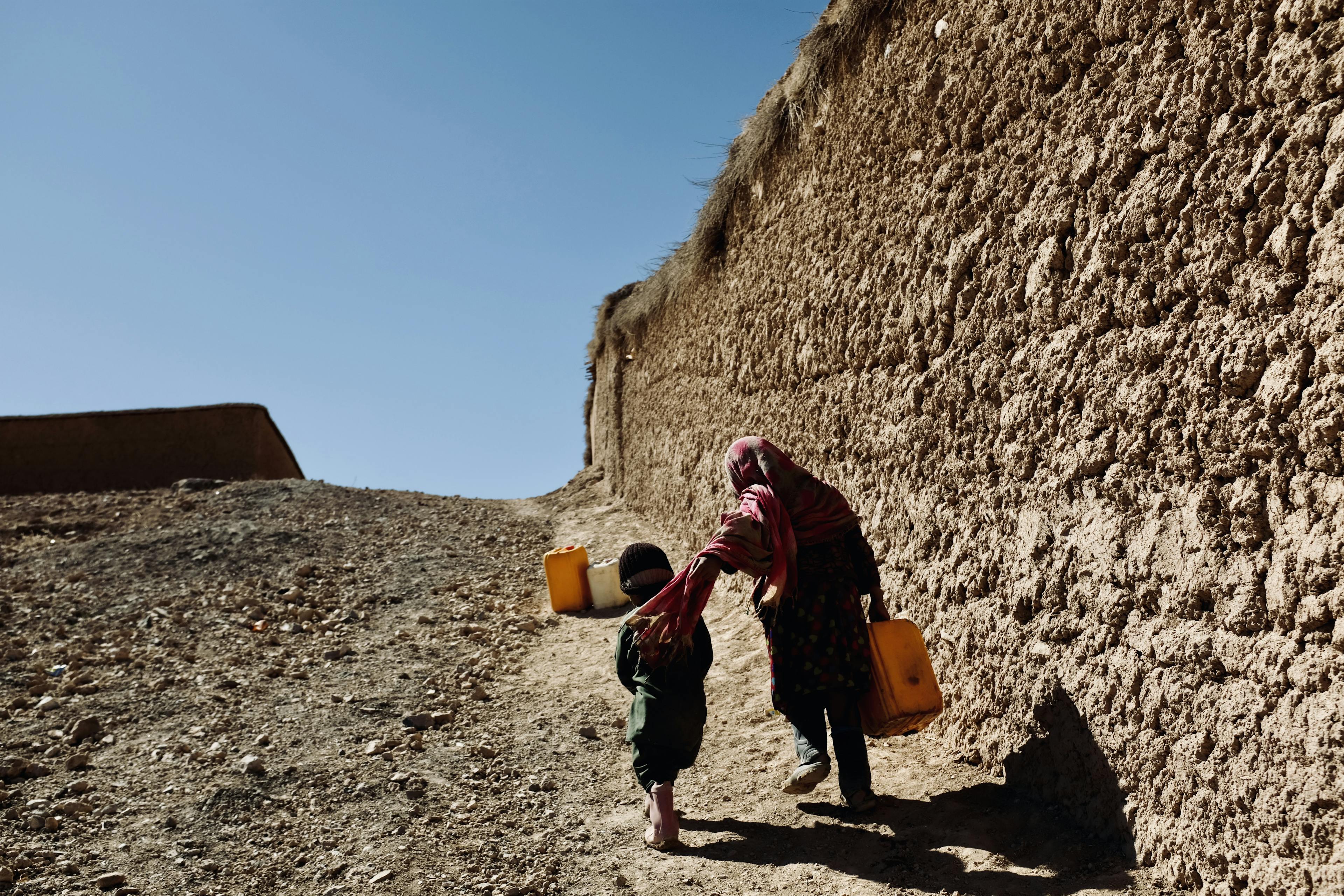 A brother and sister walk while holding jerry cans to fill with clean water.