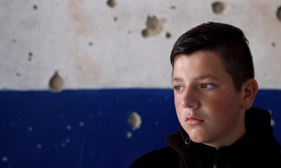 Nazar, 13, stands in front of a scarred wall in his severely damaged school in the village of Olyzarivka, Ukraine.