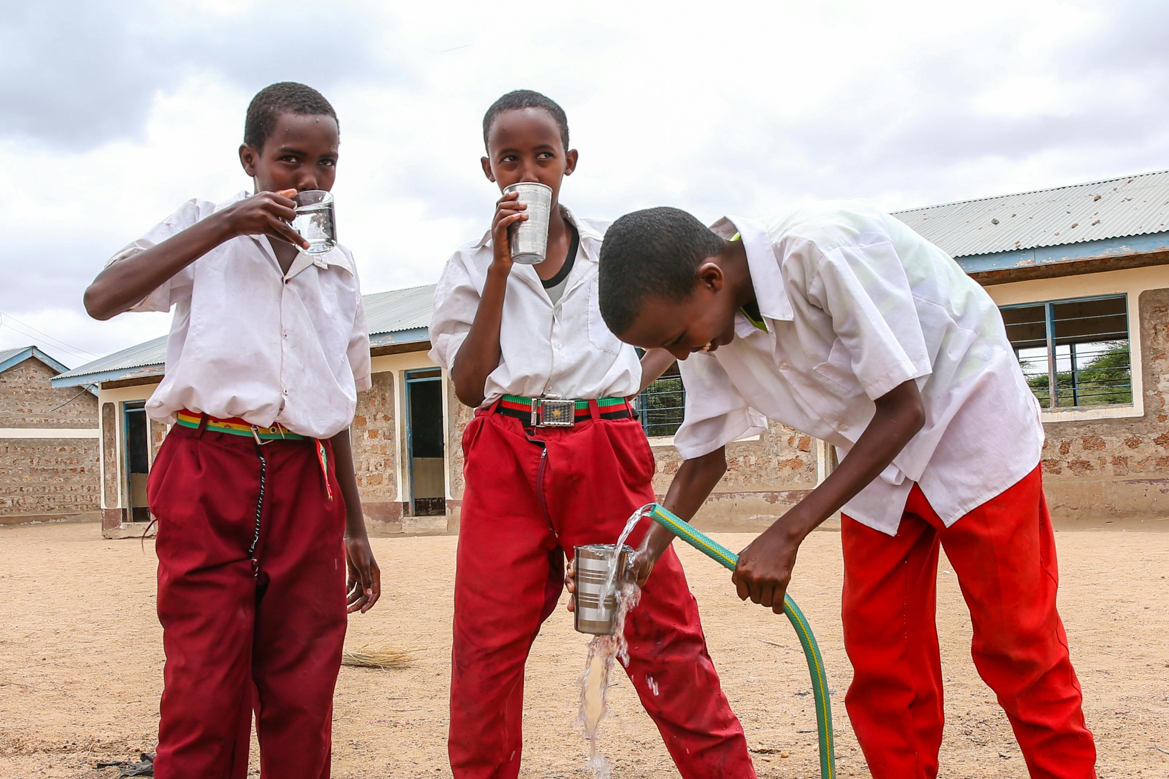 young boys filling glasses of water thanks to water system providing access to safe drinking water