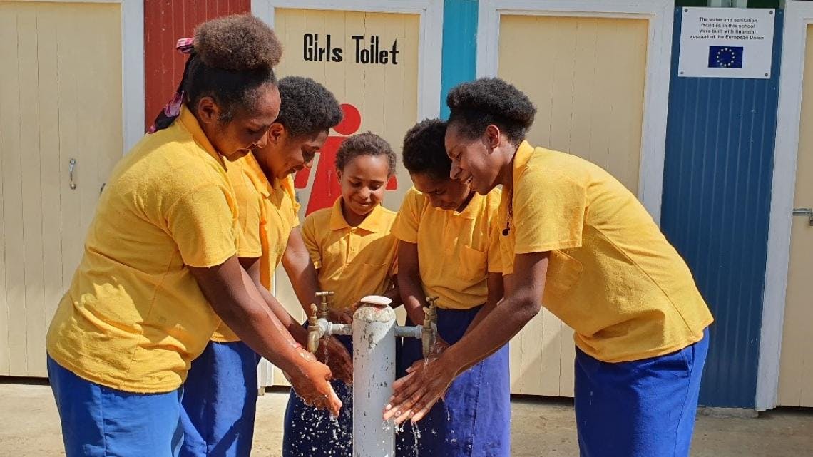 Female students washing hands at one of the three gravity-fed water points that address the schools water needs for handwashing and drinking.