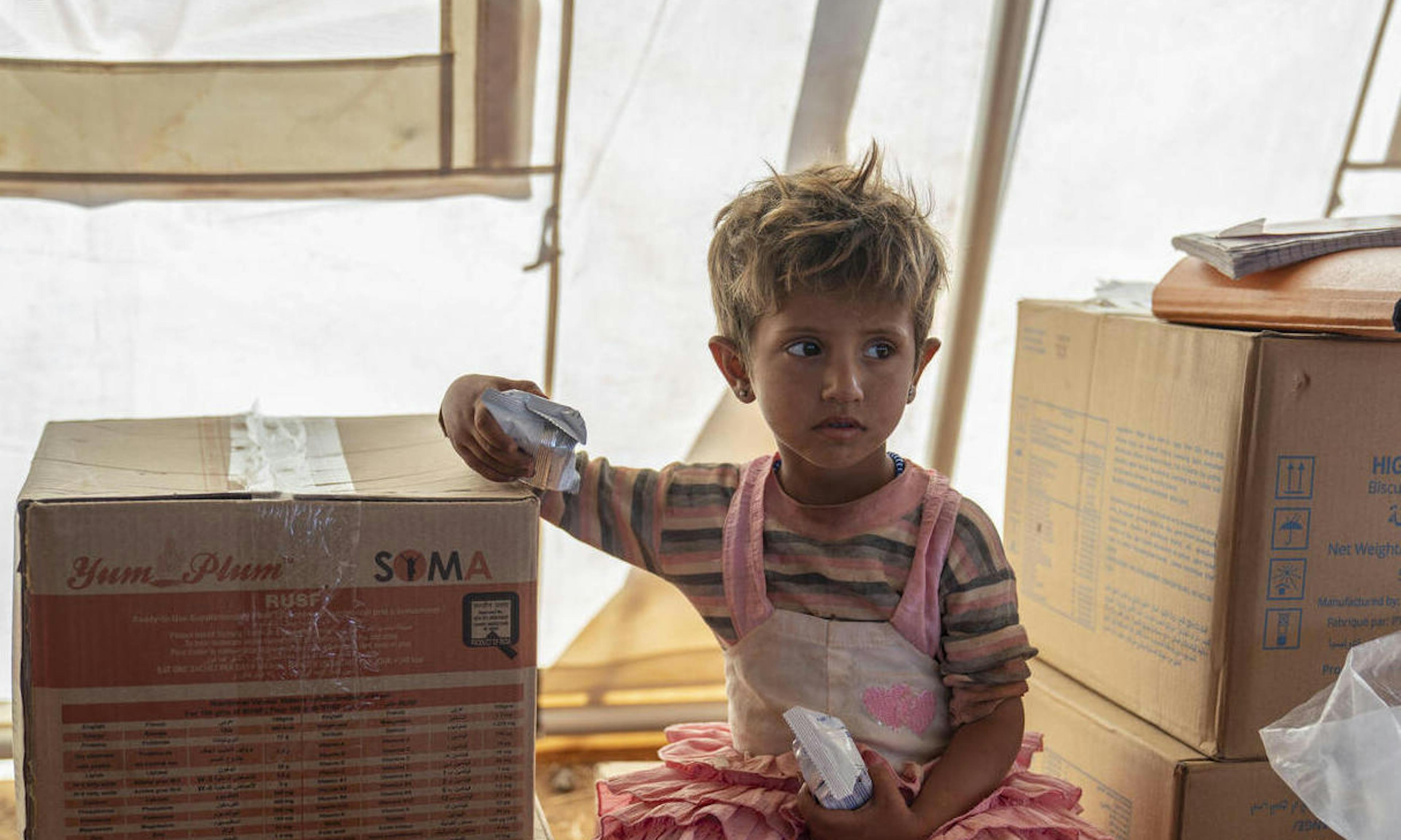 Nour, 2, holds high energy biscuits, during checkup at the UNICEF mobile health clinic, in Al-Zhuriah makeshift camp, Rural Homs, Syria.