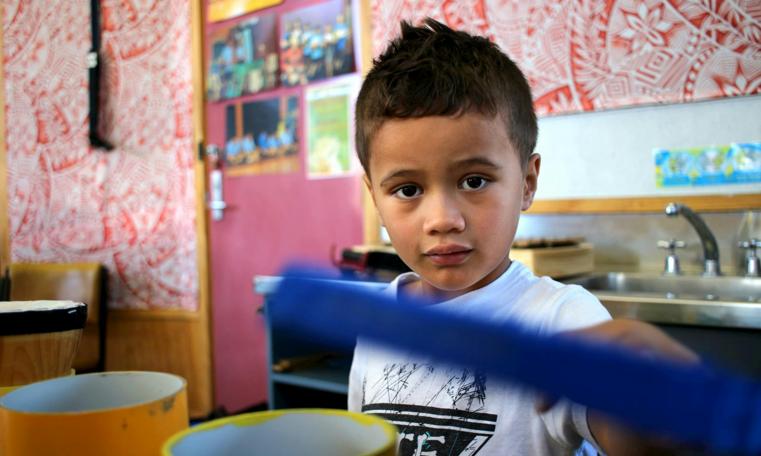 A young Māori boy looks at the camera while standing in a classroom