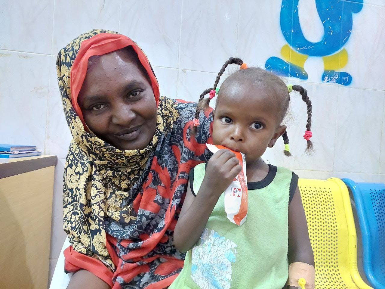 On 1 June, 3-year-old daughter, AlBatoul Taj-Elsir sits on her mother's lap as she eats ready-to-use-therapeutic food (RUTF) in the nutrition ward at Dongola specialized hospital, where she is receiving treatment for severe acute malnutrition.
