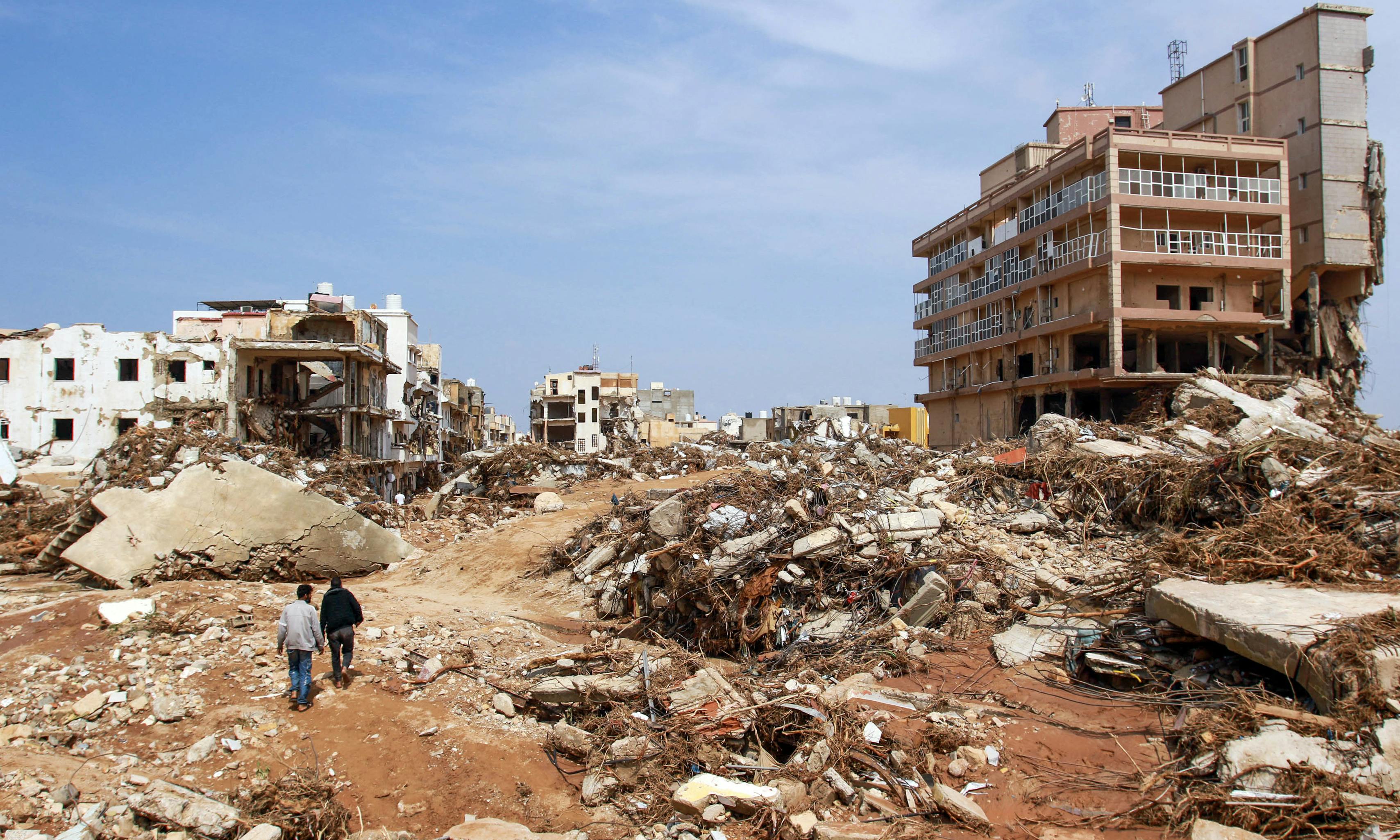 Men walk past debris of buildings caused by flash floods in Derna, eastern Libya. The floods on September 11, 2023 have killed more than 2,300 people.