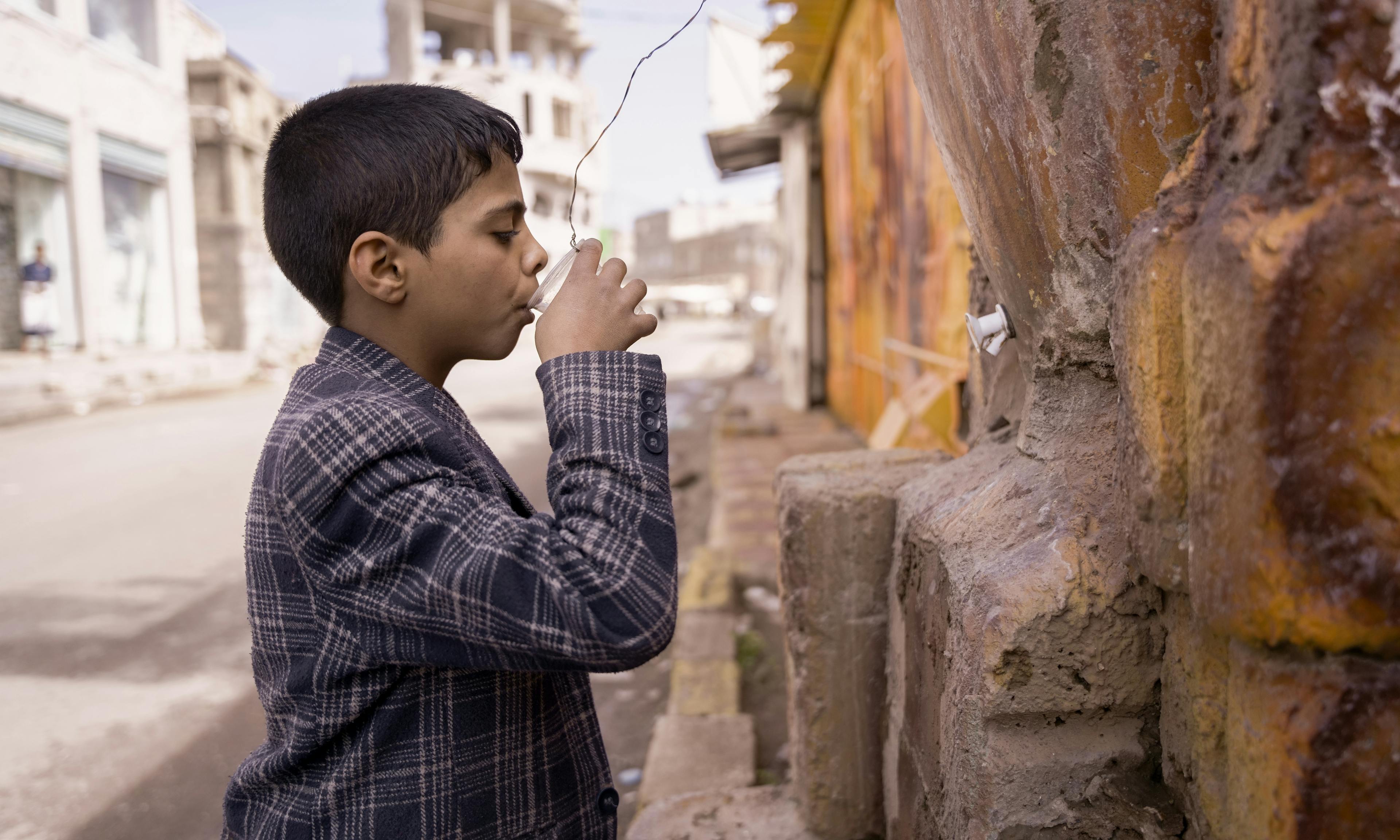 A child is pictured drinking water from a public clay cooler in Dhamar Governorate, Yemen. The availability of clean water is a critical issue in Yemen, where many communities lack access to safe drinking water.