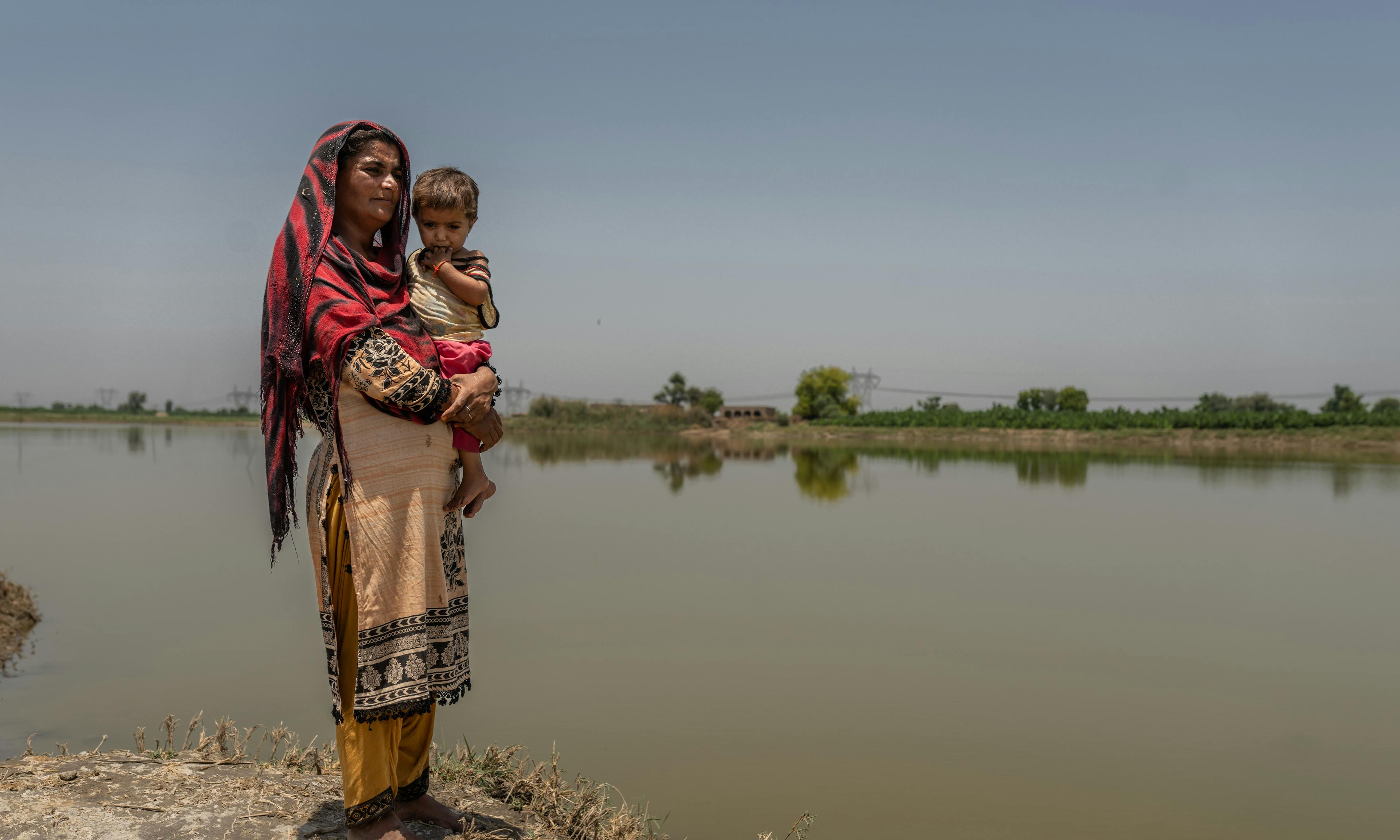 A mother holds her baby next to flooded areas in Village Balocho Zardari, Shaheed Benazirabad, Sindh, Pakistan.