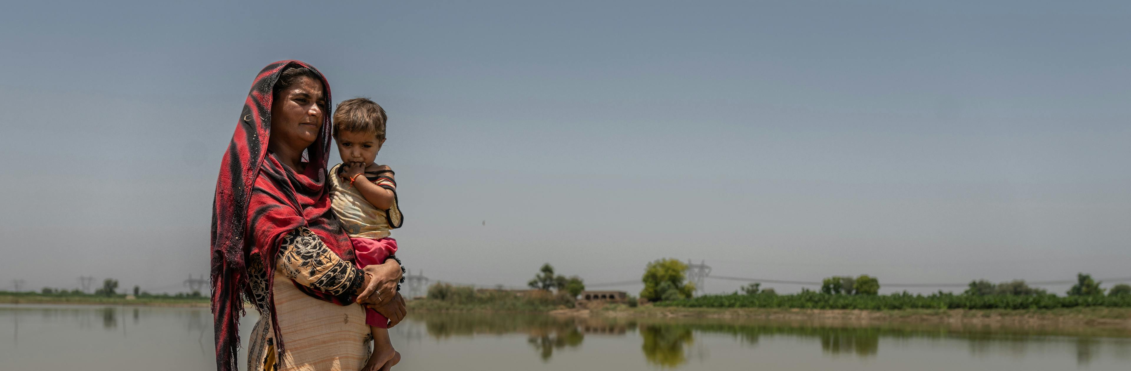 A mother holds her baby next to flooded areas in Village Balocho Zardari, Shaheed Benazirabad, Sindh, Pakistan.