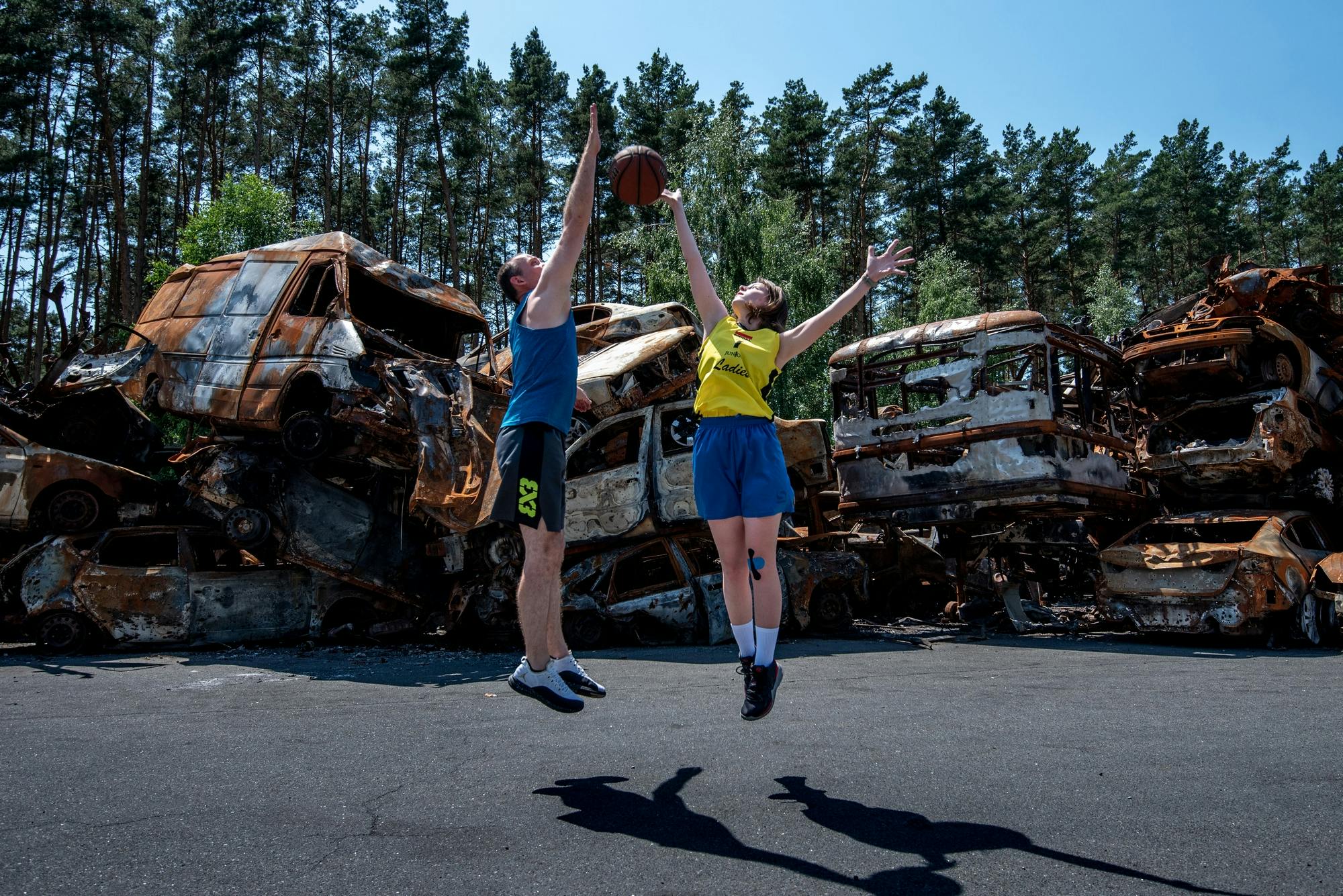 In Irpin, a Kyiv suburb, there are a lot of burned out cars with a wall made out of them, so that a road is visible. Next to them, there is a space big enough to play basketball on.