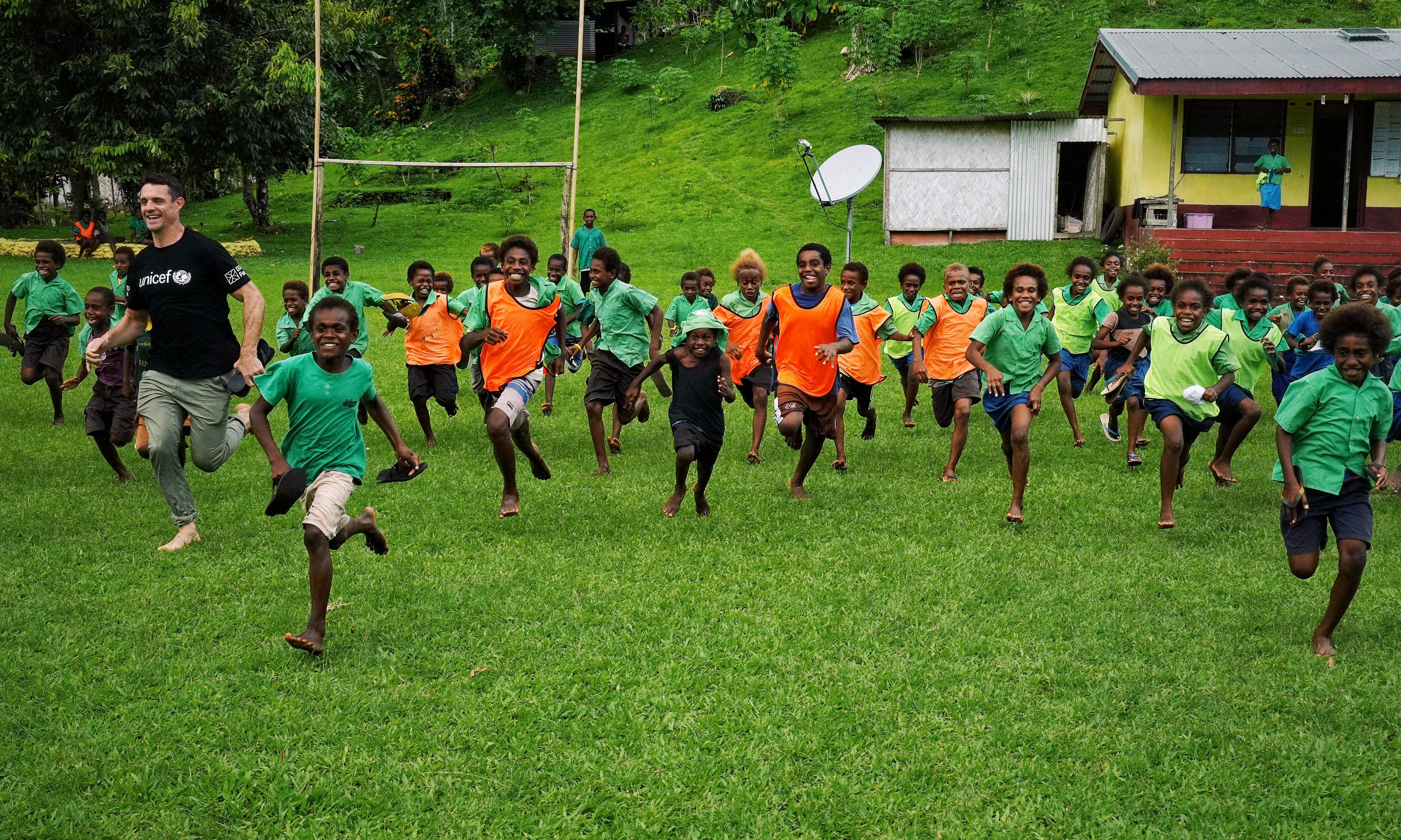 Dan Carter and school kids in Vanuatu playing rugby on the field