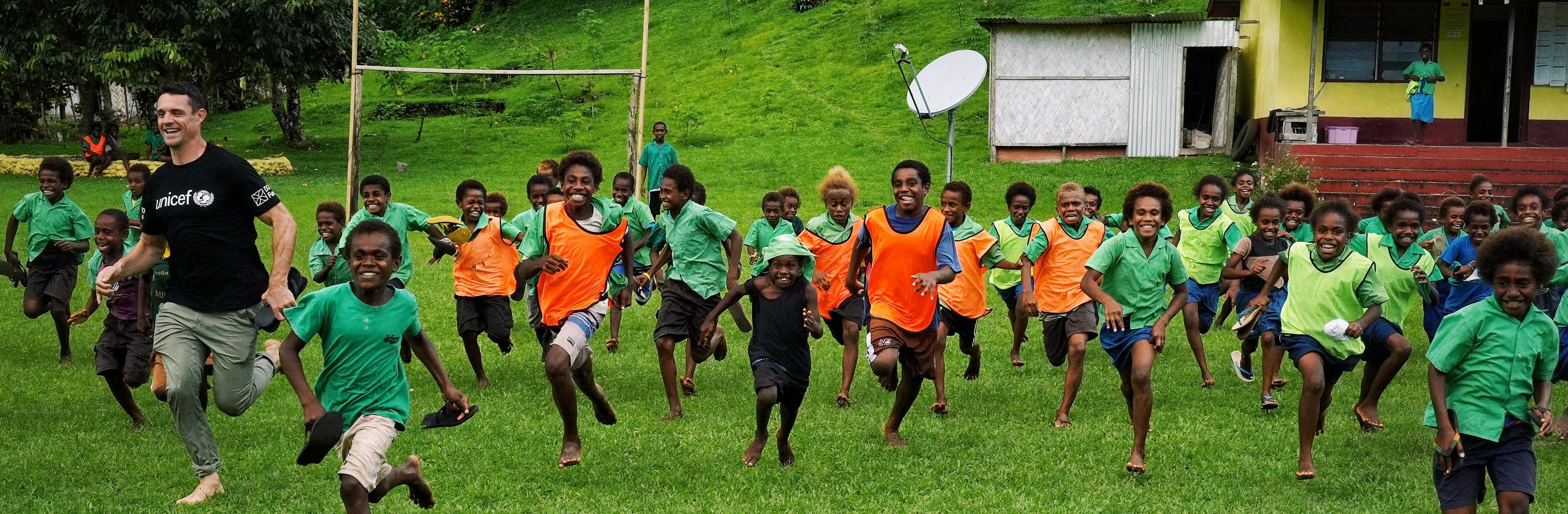 Dan Carter and school kids in Vanuatu playing rugby on the field