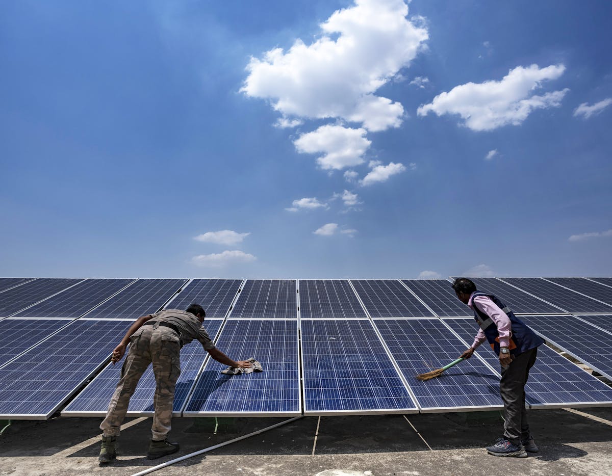 Workers clean the solar panels for the solar cold chain point installed on the rooftop of the Health and Wellness Centre in Pithoria, Jharkhand state, India