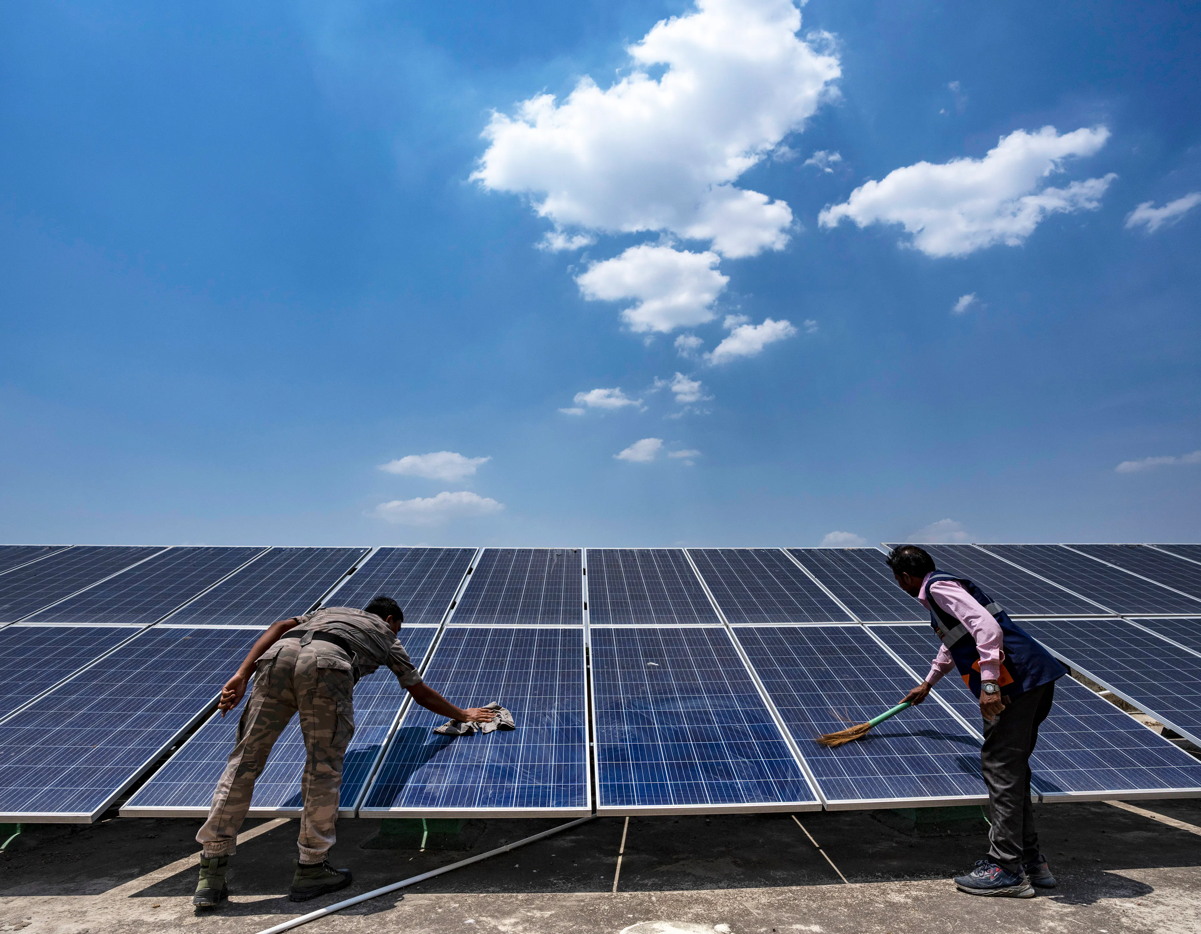 Workers clean the solar panels for the solar cold chain point installed on the rooftop of the Health and Wellness Centre in Pithoria, Jharkhand state, India