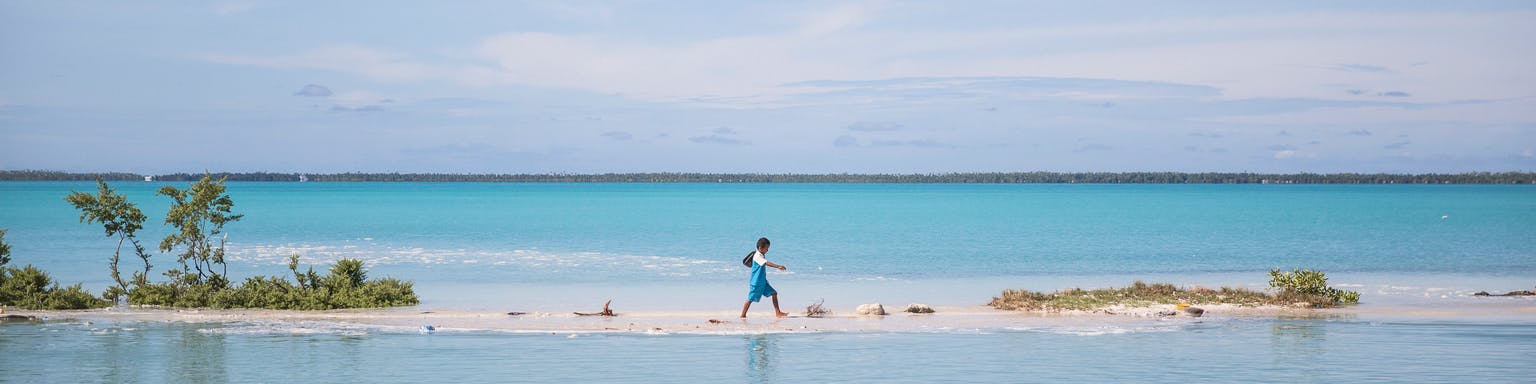 A boy walking across a piece of land surrounded by water. 