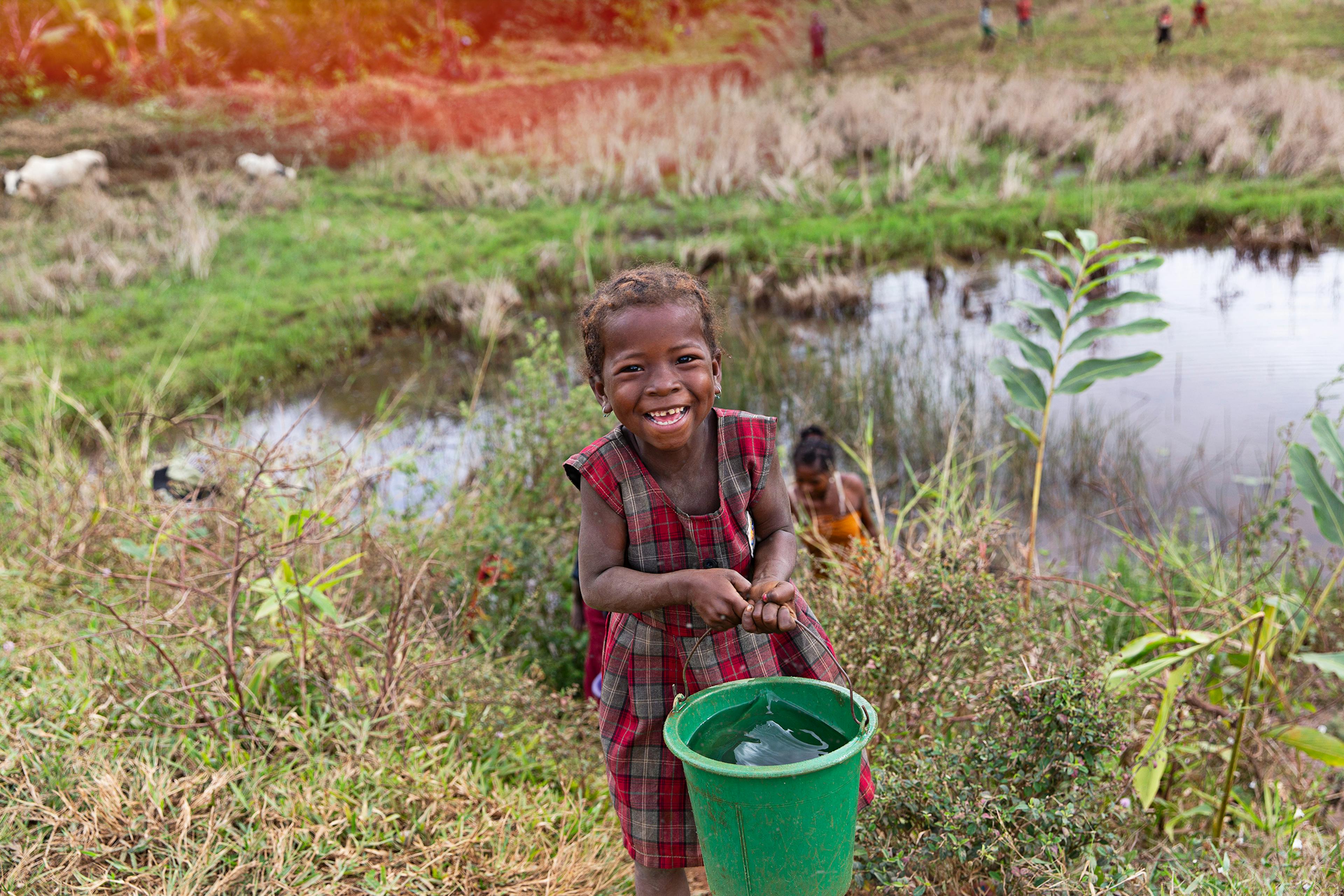 young child holds bucket of water at the side of a swamp