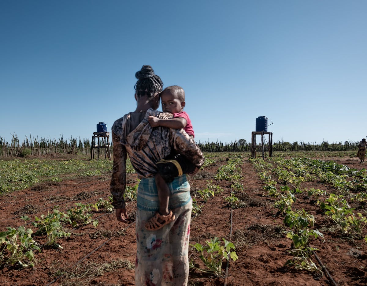 A mum holding her child walking through the the vegetable garden that is part of the "Multiple Use of Water" System in Ehavo Public Primary School in Madagascar.