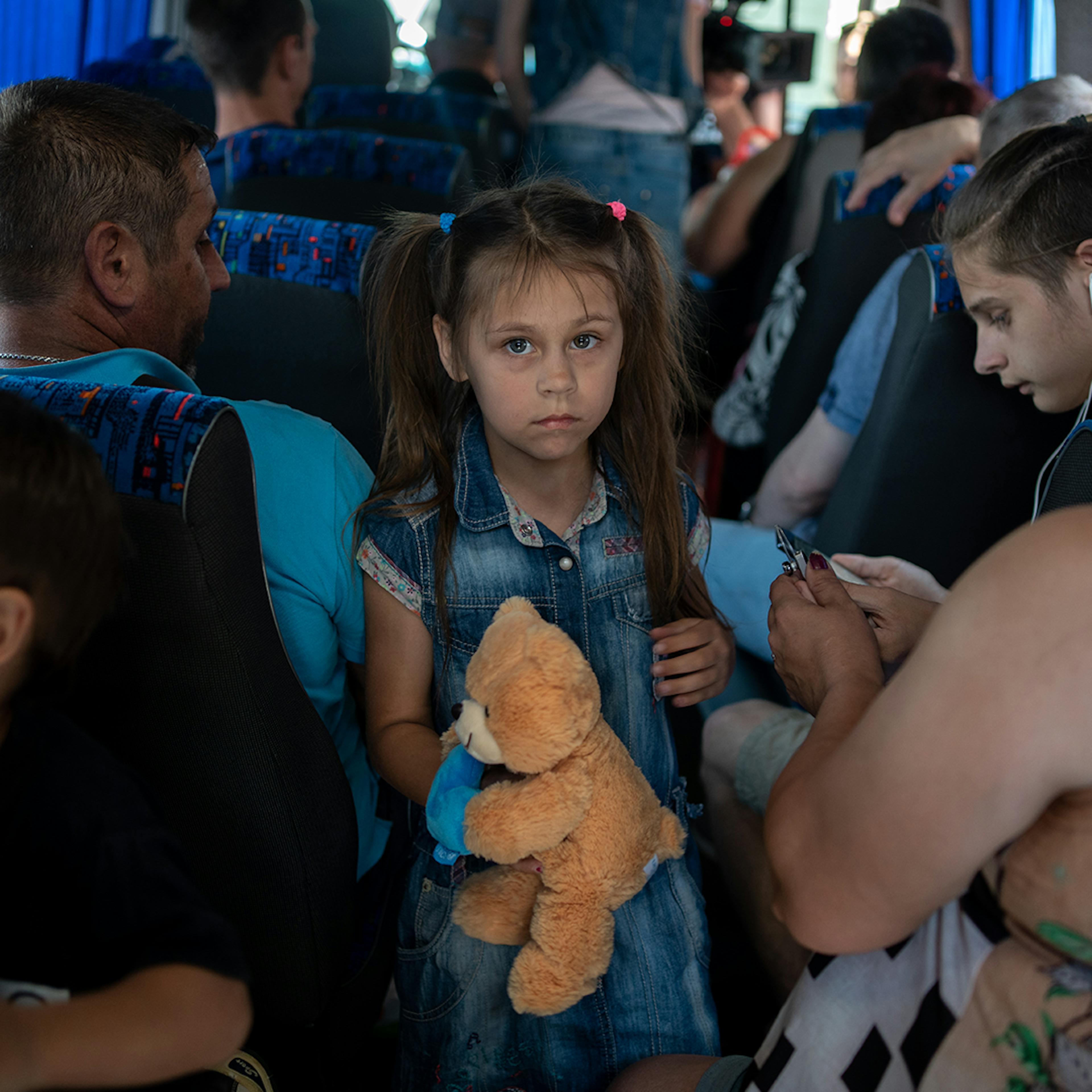 June 7, 2023. Kherson, Ukraine. Dmytro, a father of five children (on the left with his back), his daughter Anya, 7 years old, and his son Ernest, 15 years old (on the right, wearing headphones) are in the evacuation bus at the Kherson bus station.