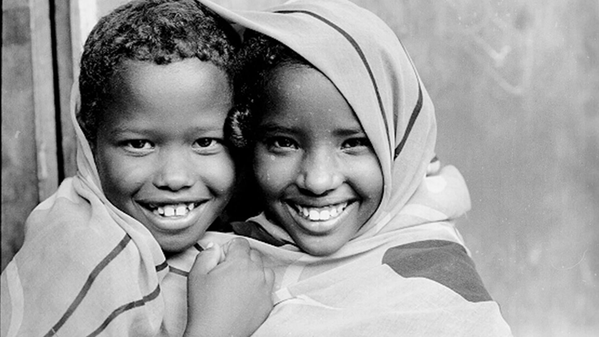 A boy and a girl hug each other and happily shares the same head cover. 2001.