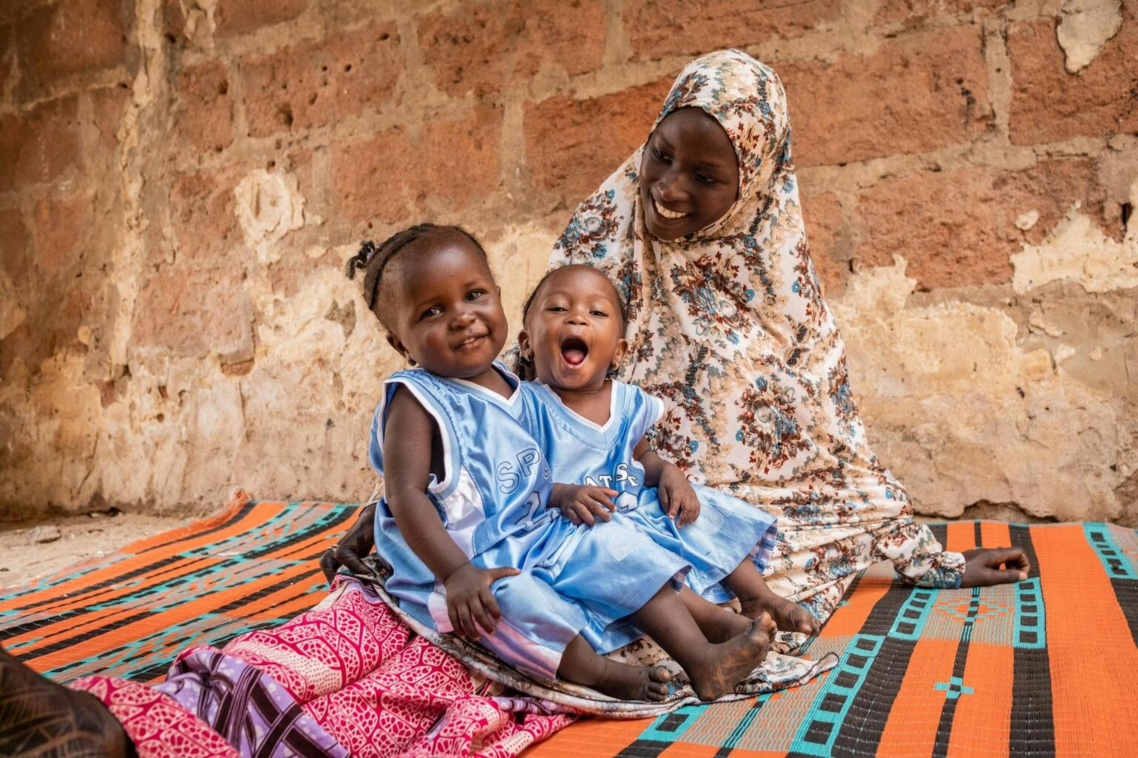 Catching signs of malnutrition early - twin girls sit with their mother after recovering from severe acute malnutrition.