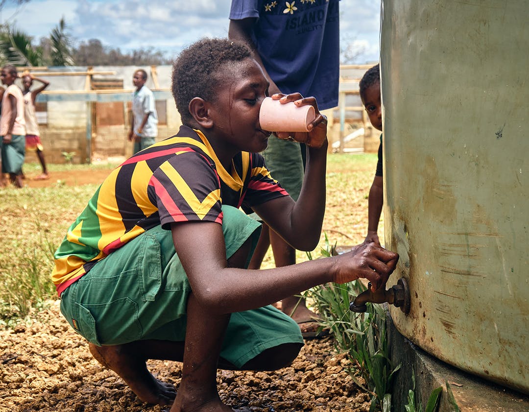 A boy drinking water from rainwater tank.