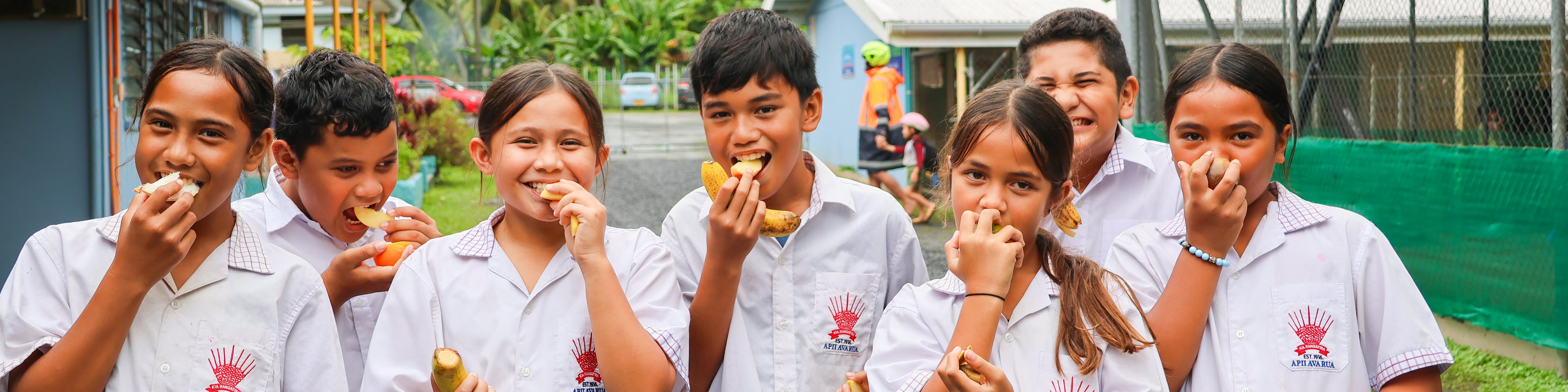 Children of Apii Avarua Primary School enjoying local fruits. The students actively participate in an initiative that emphasizes the importance of eating and appreciating local fruits and vegetables. By bringing a fruit each week, the school aims to encourage children to develop a love for nutritious foods.