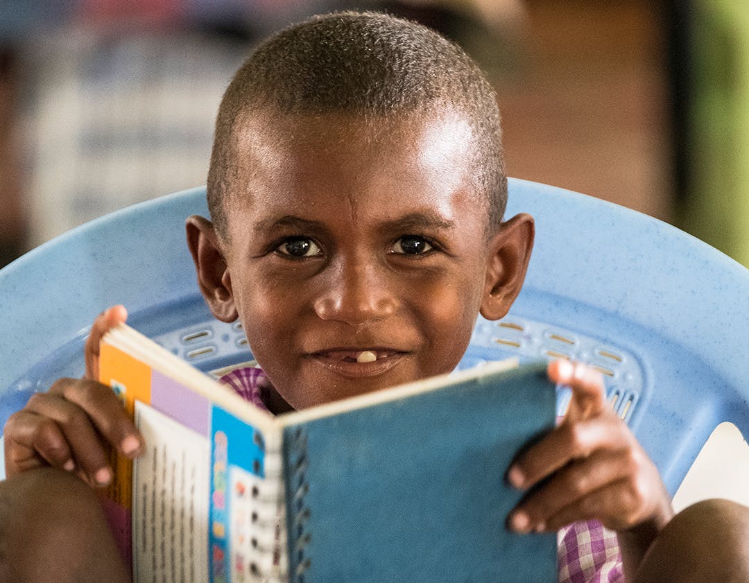 A male student of Vitu Primary School smiling and holding his book in a classroom. Guadalcanal Province, Solomon Islands.