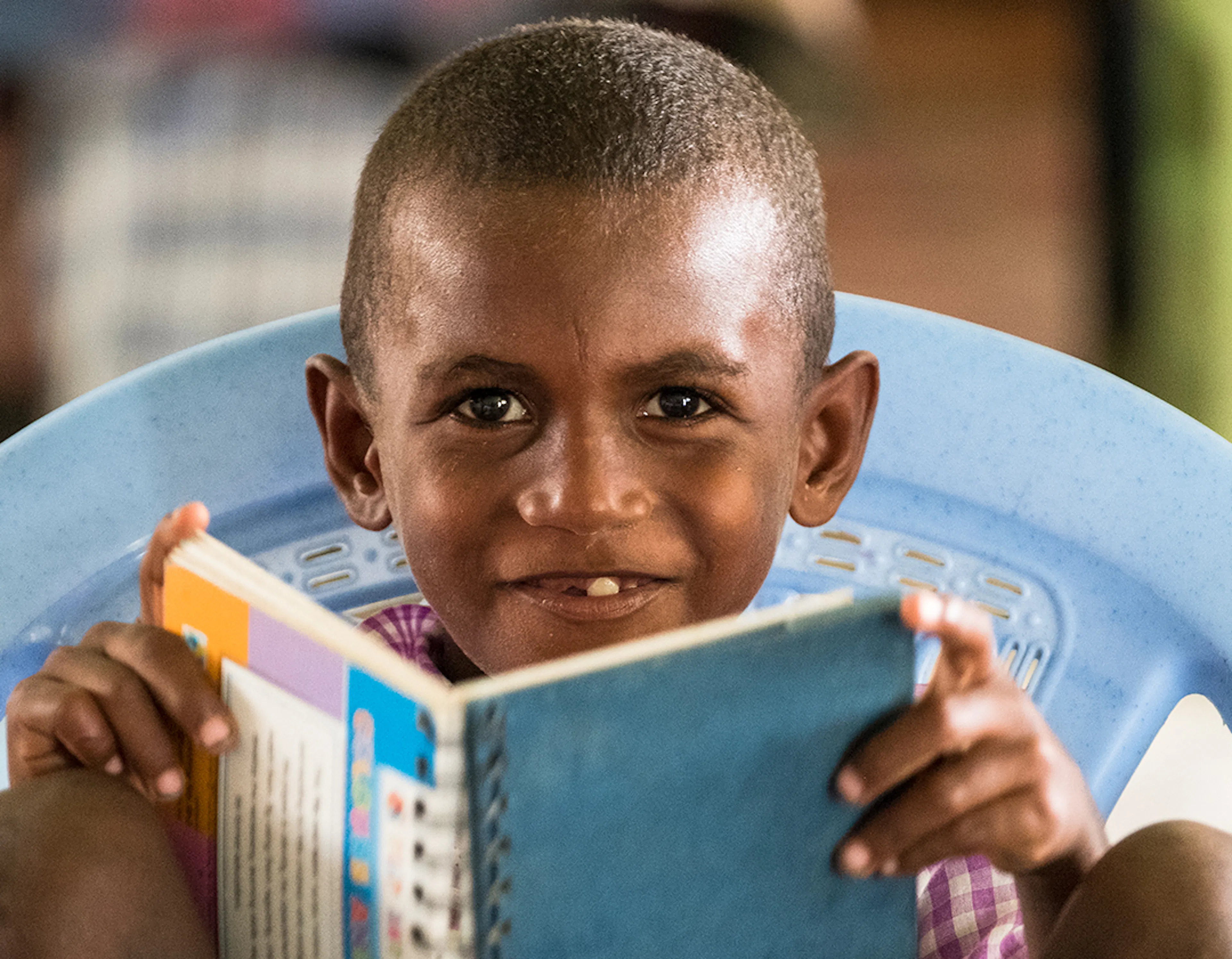 A male student of Vitu Primary School smiling and holding his book in a classroom. Guadalcanal Province, Solomon Islands.