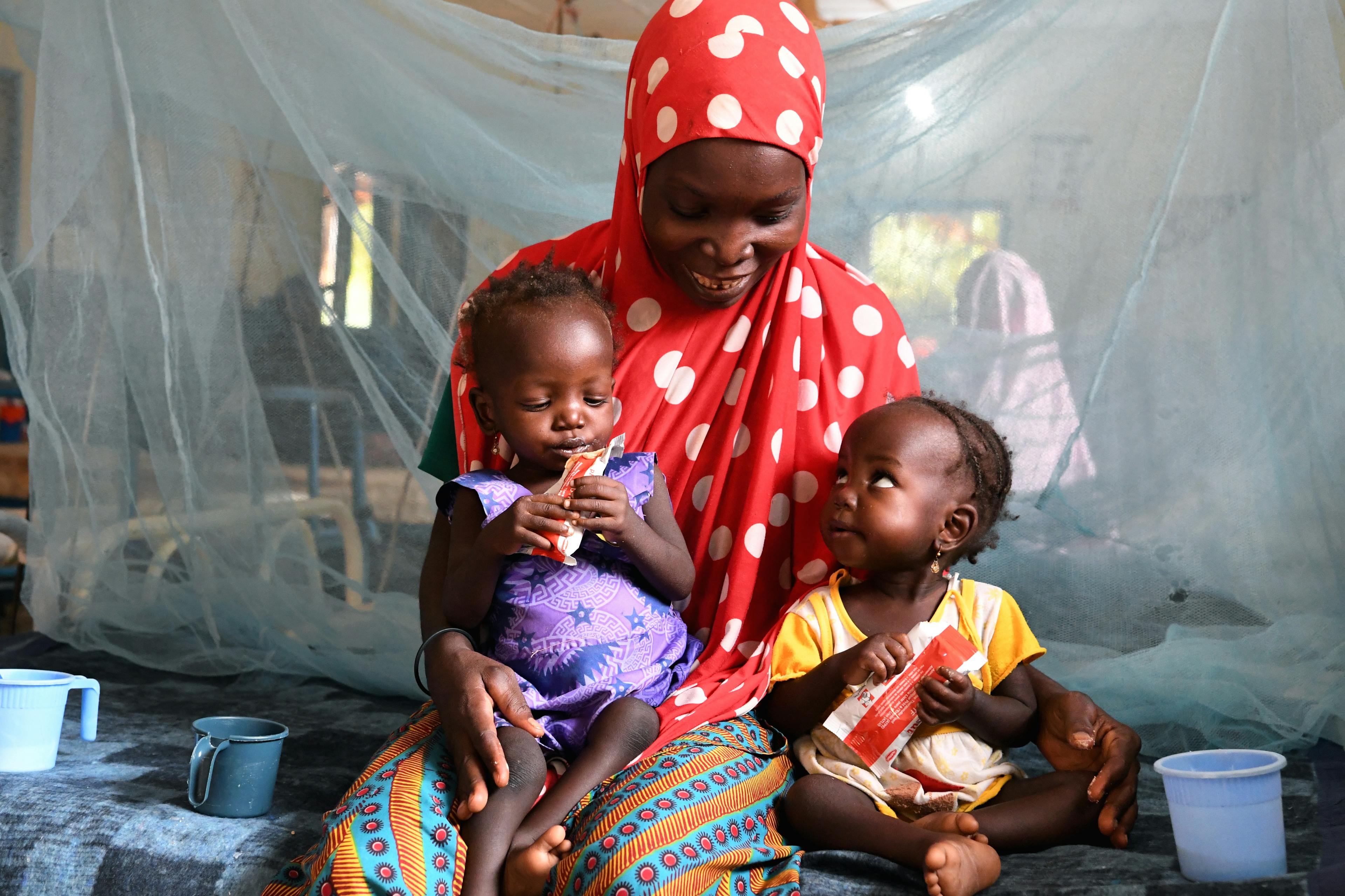 On 9 October 2021 in Niger, Nana Hadiza, 28, holds her twin daughters as they sit on a hospital bed at the CHU Hospital of Maradi. The twins are treated for malnutrition with Ready-to-Use Therapeutic Foods (RUTF) like Plumpy'Nut and H100 supplements.