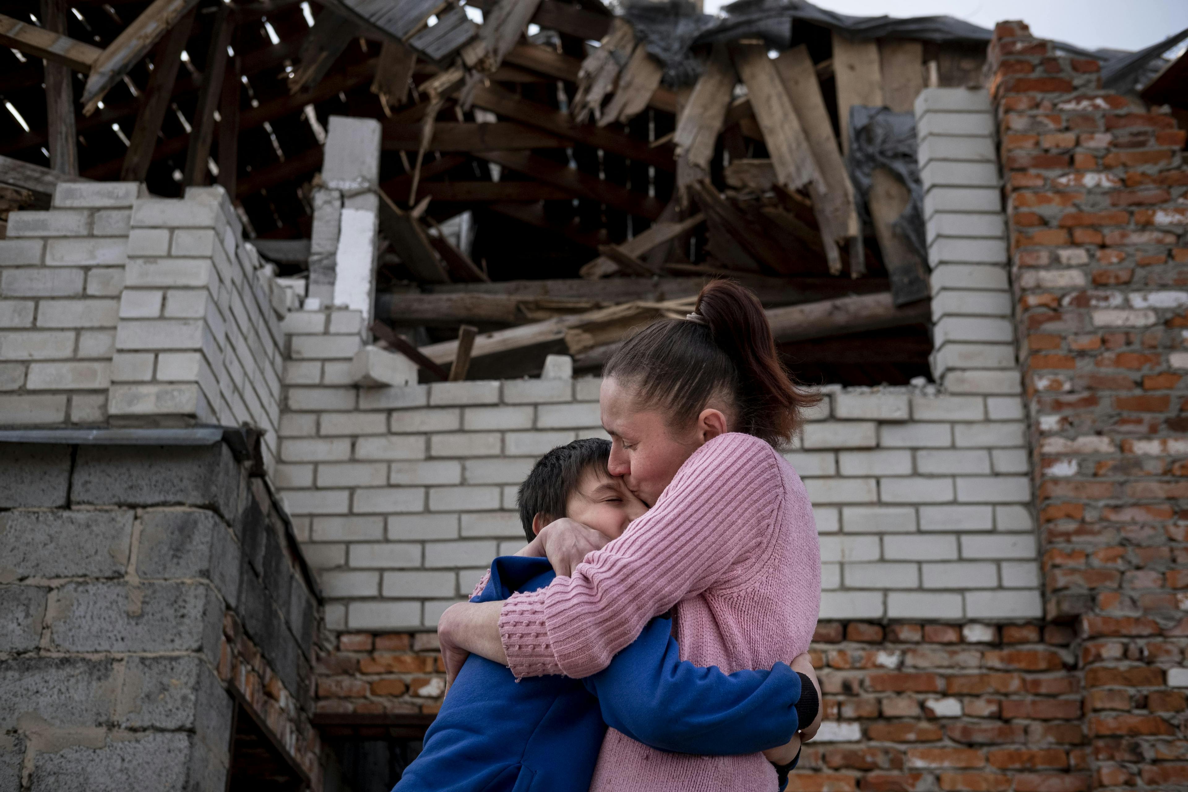 Corporate Partnerships- In Ukraine, Olena, 43, holds her son, Mikhailo, 9, in a tight embrace, and kisses him, in front of their damaged home in Novoselivka, outside of Chernihiv