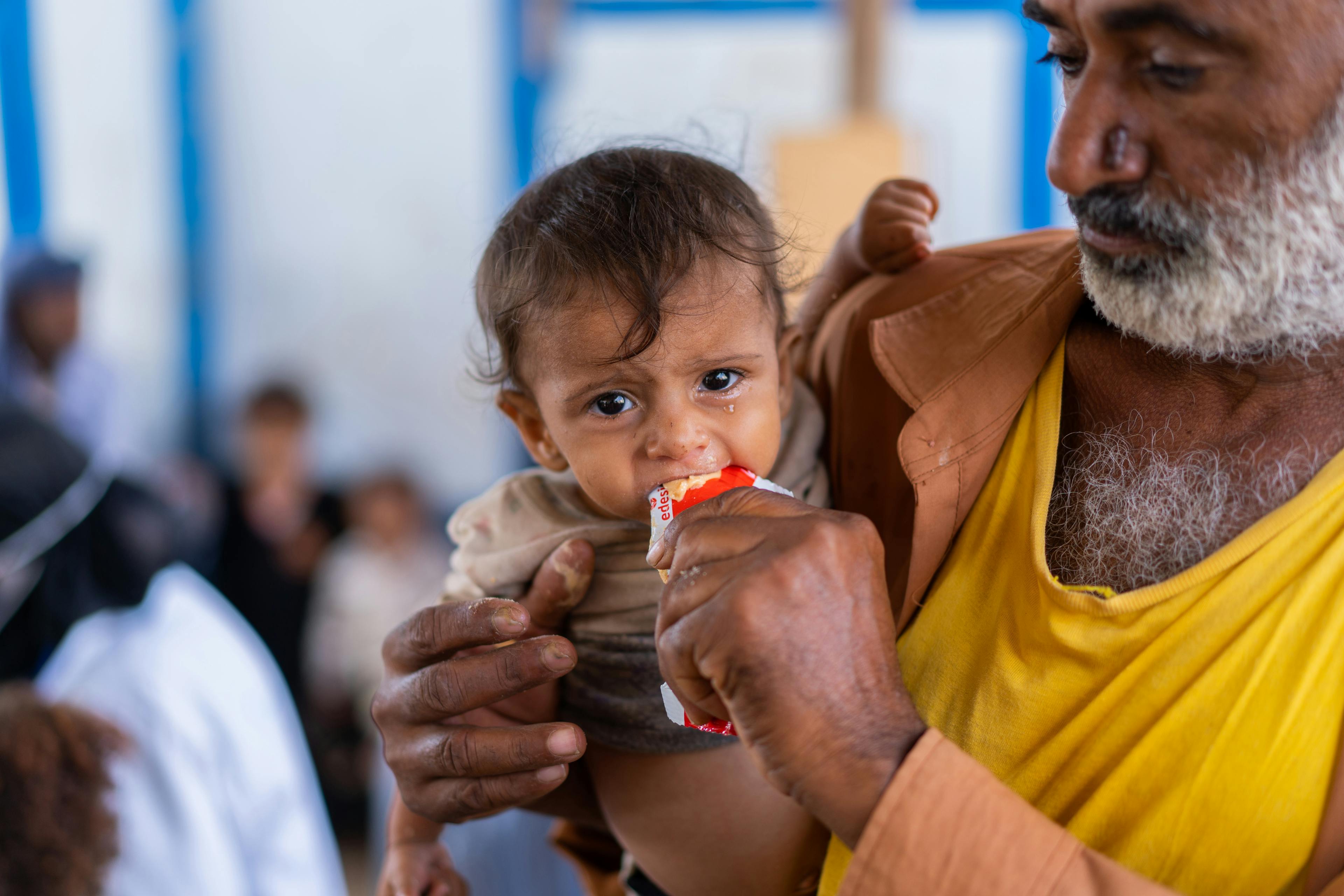 On 10 January 2023, a child eats from a sachet of Ready-to-Use Therapeutic Food (RUTF) while his father holds him in Al-Sha’ab, a camp for internally displaced persons in Al Buraiqeh District, Aden Governorate, Yemen.