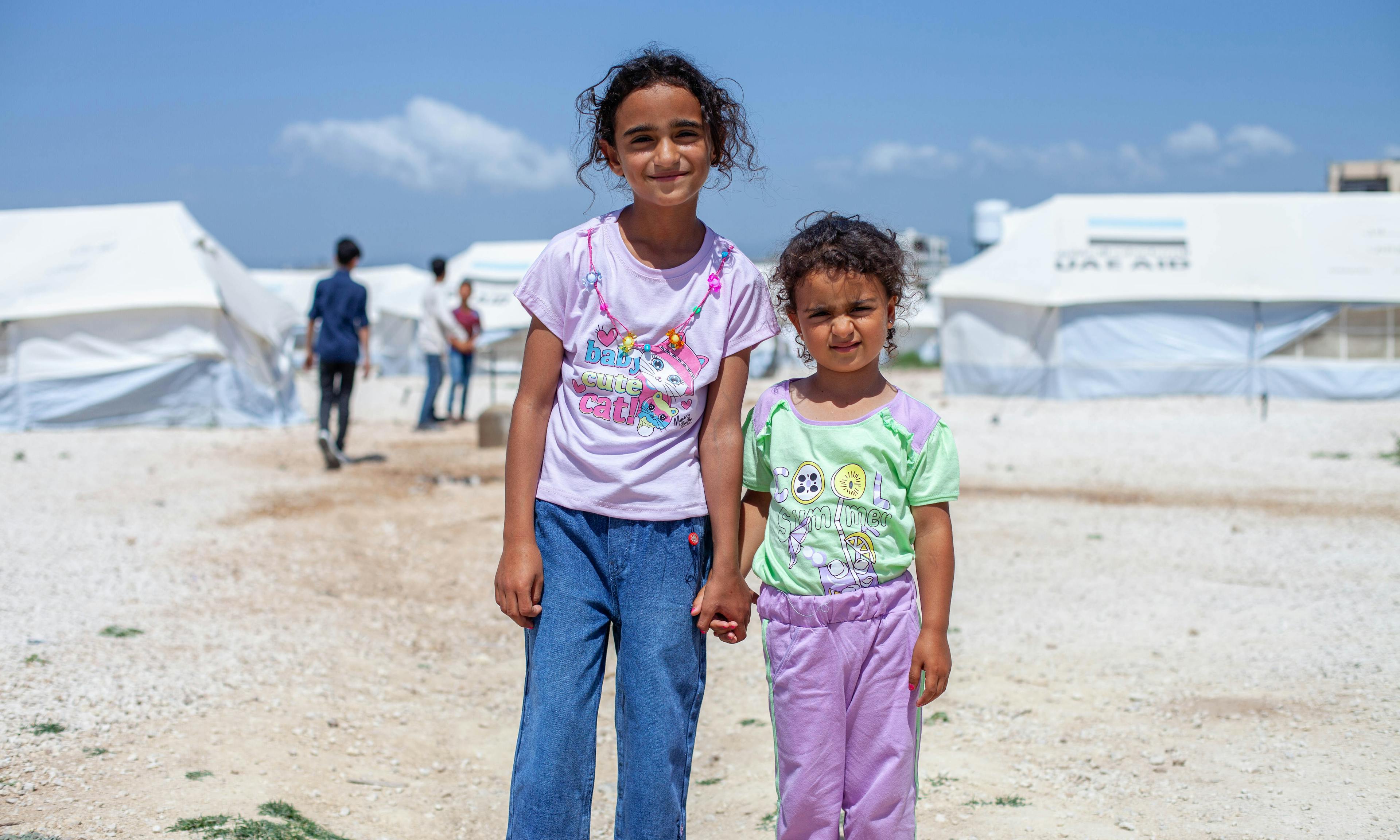 Two sisters hold hands at a refugee camp in Syria: Syrian children amidst the challenges of conflict, receiving support from UNICEF Aotearoa.