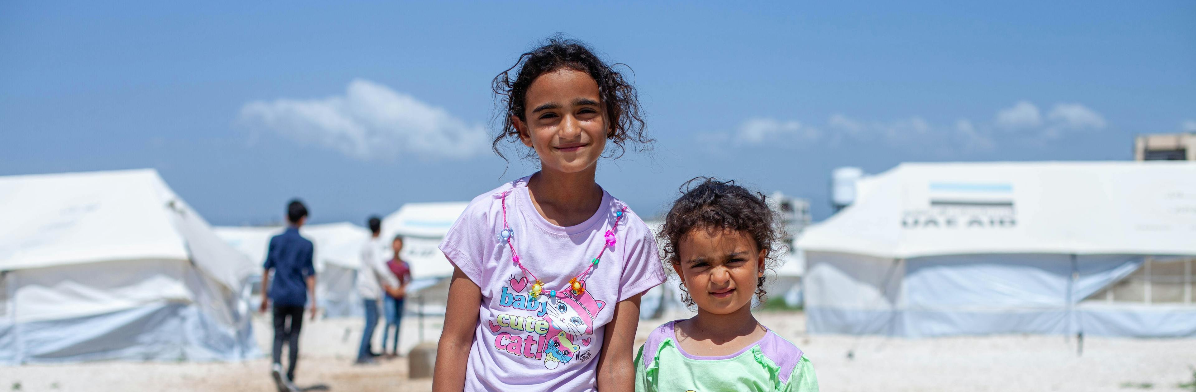 Two sisters hold hands at a refugee camp in Syria: Syrian children amidst the challenges of conflict, receiving support from UNICEF Aotearoa.