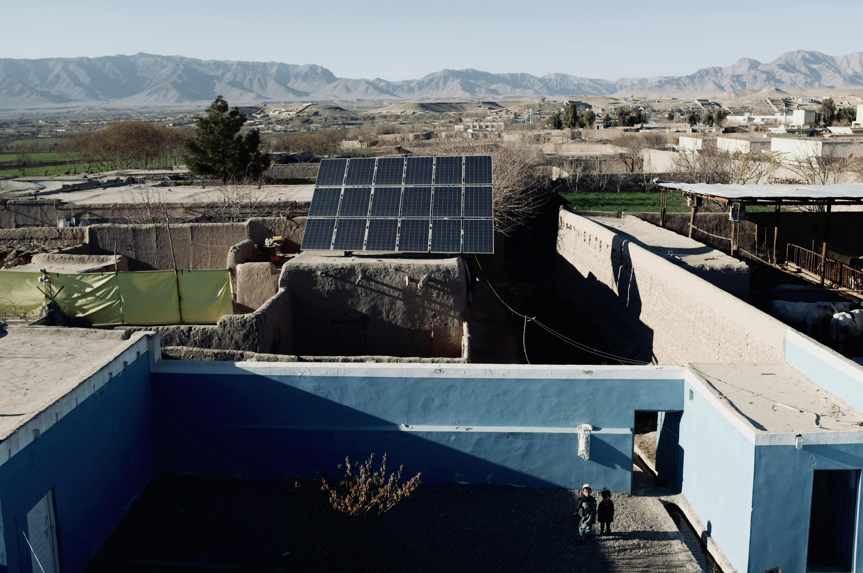 Two children stand in the green space of the solar powered water house in Sahibzada Village. The tower was built in 2001 and operates by 18 solar panels. The mountains of Uruzgan Province can be seen in the back.