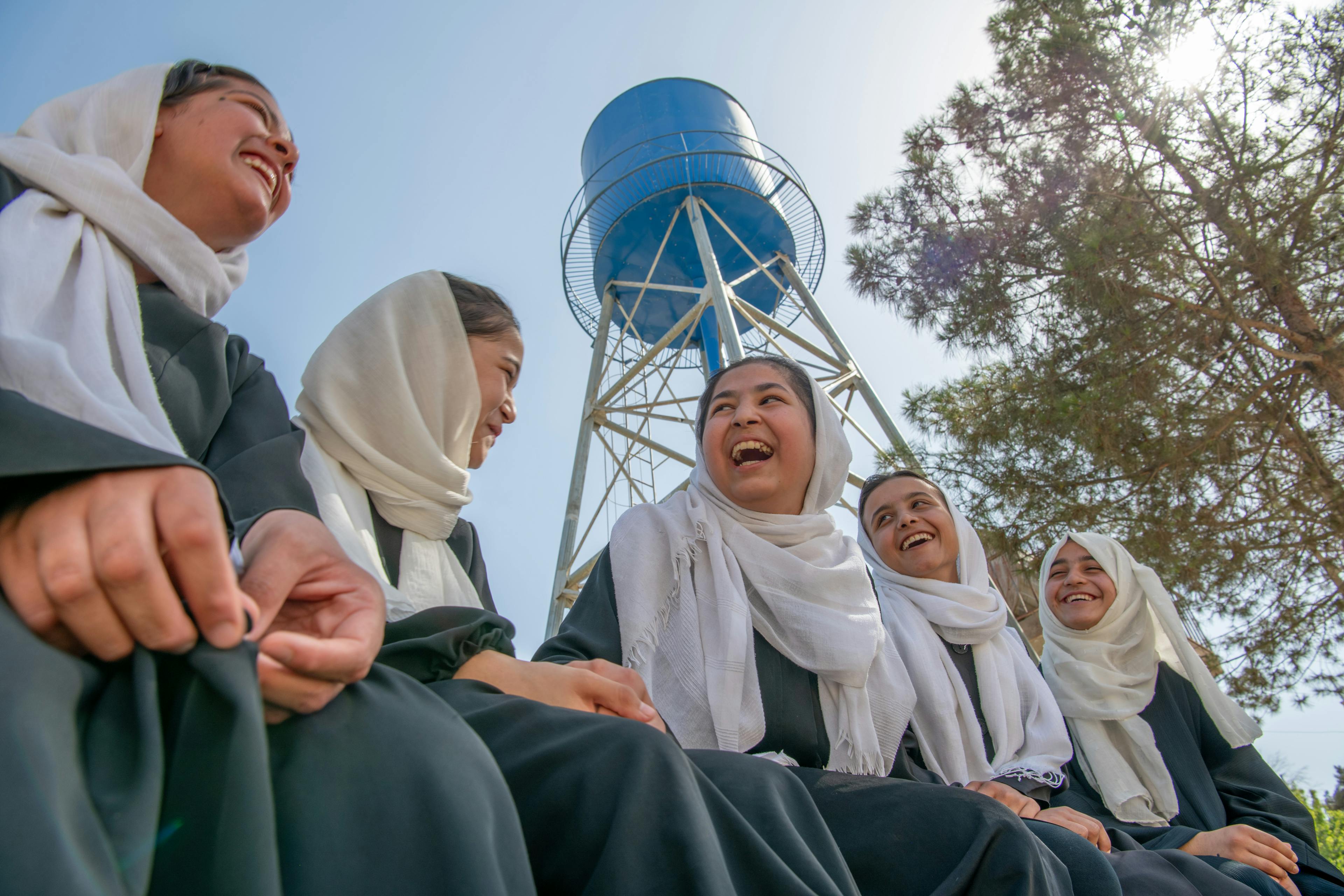 Global parent- A group of students talk and laugh near the UNICEF-installed water tank at Mawlana Jalaluddin Mohammad Balkhi School in Mazar-i-Sharīf, Balkh Province, Afghanistan.