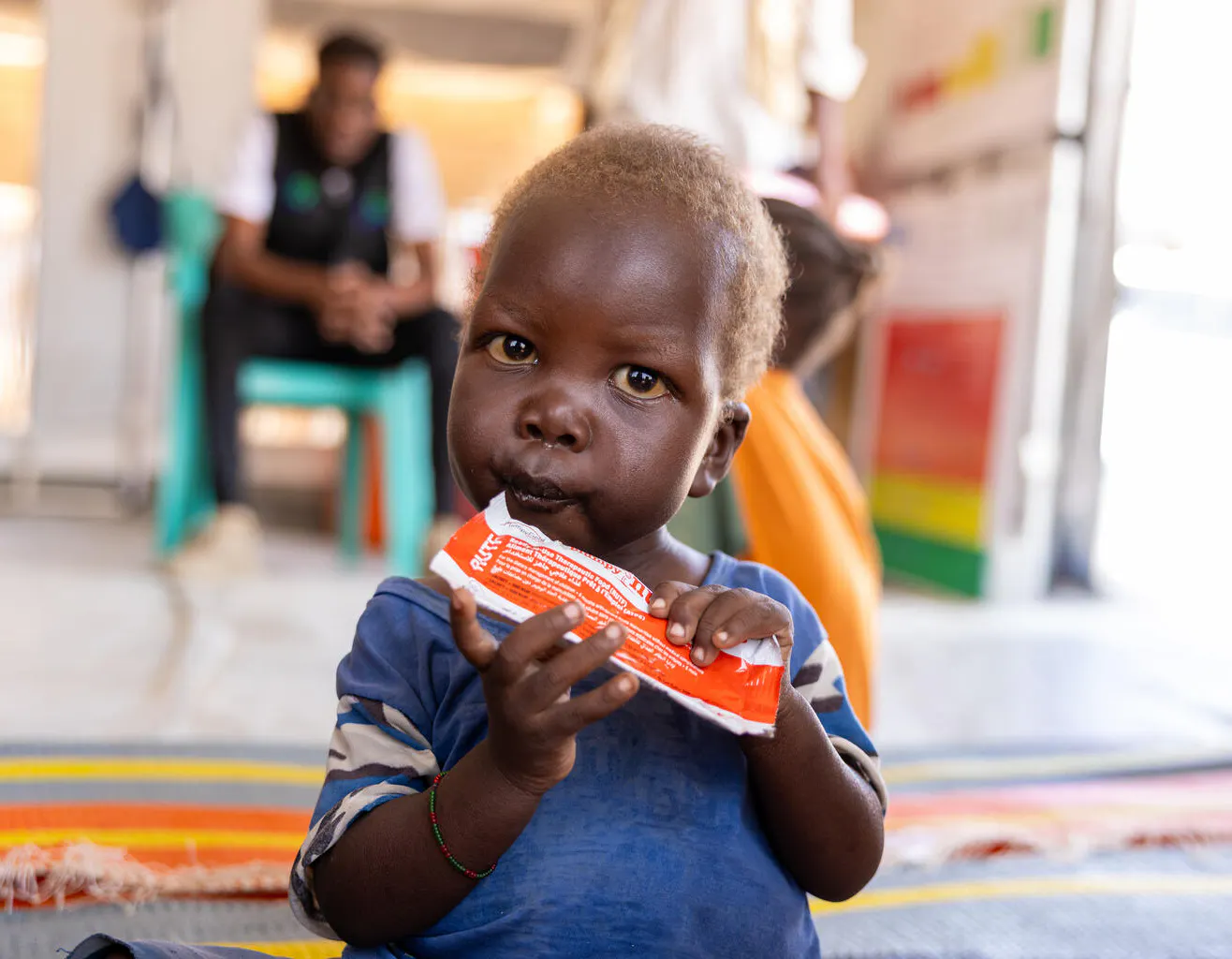 20-month-old Mujahid eats ready-to-use-therapeutic food (RUTF) during a follow up visit at the outpatient nutrition unit in Goz Alsalam IDP site in White Nile State.