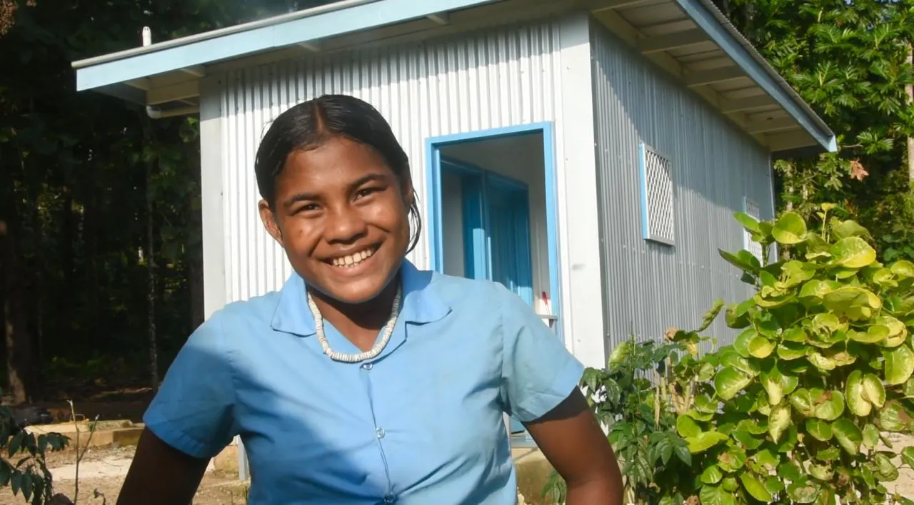 A student stands in front of a WASH facility at a school in the Solomon Islands