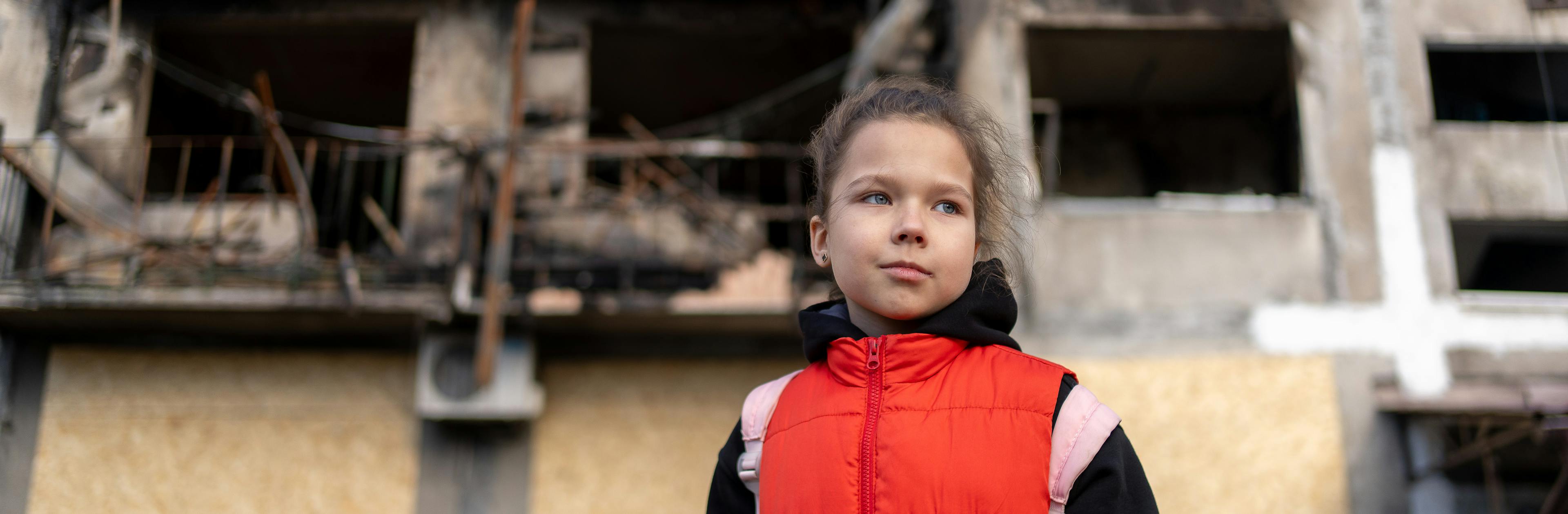 12 March 2025, Dobropillia, eastern Ukraine. Eight-year-old Myroslava stands in front of a bombed-out residential building, one of several damaged in a missile strike on 7 March.